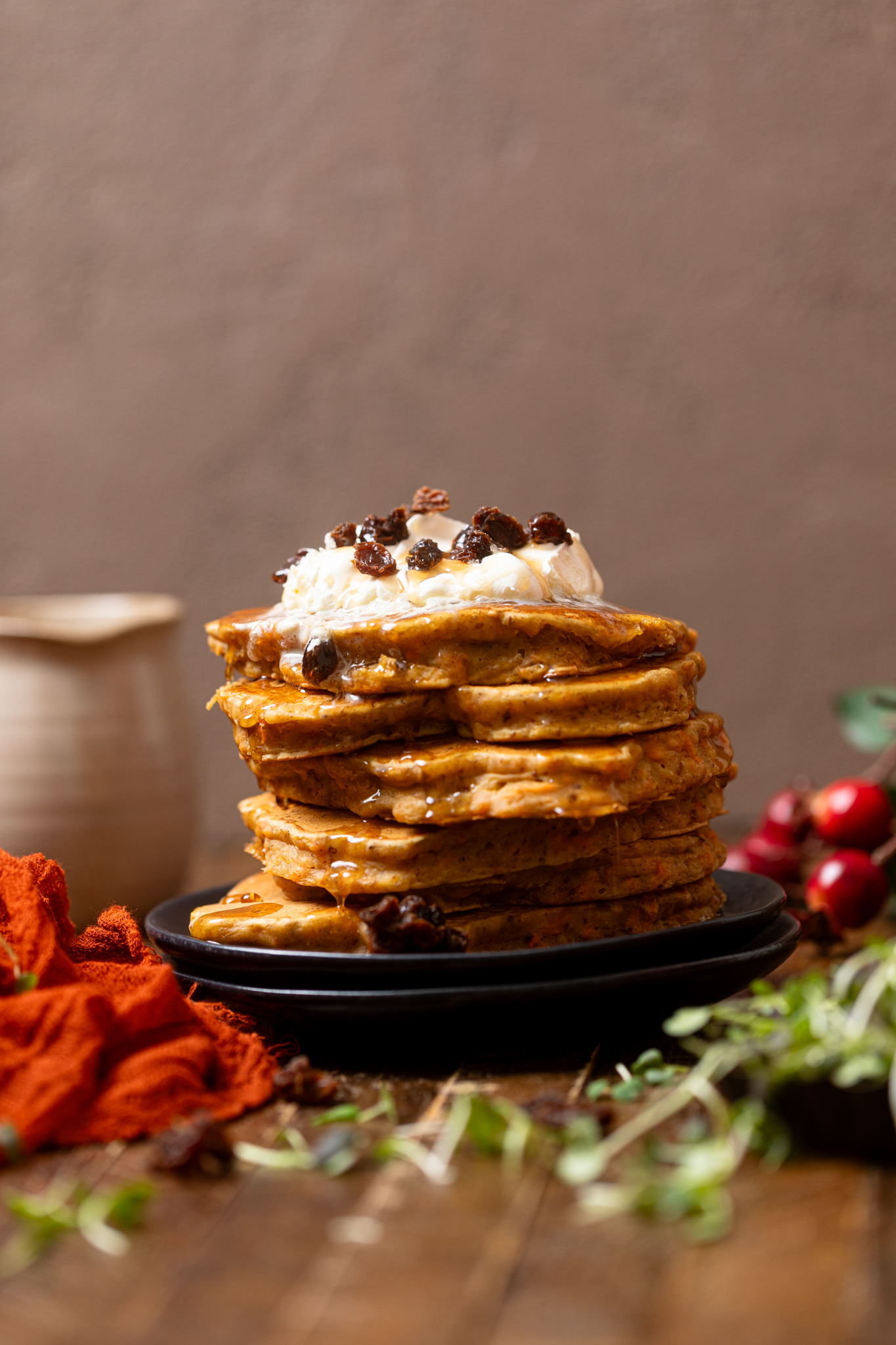 The Best Vegan Carrot Cake Pancakes stacked on black plates with toppings and a red napkin.