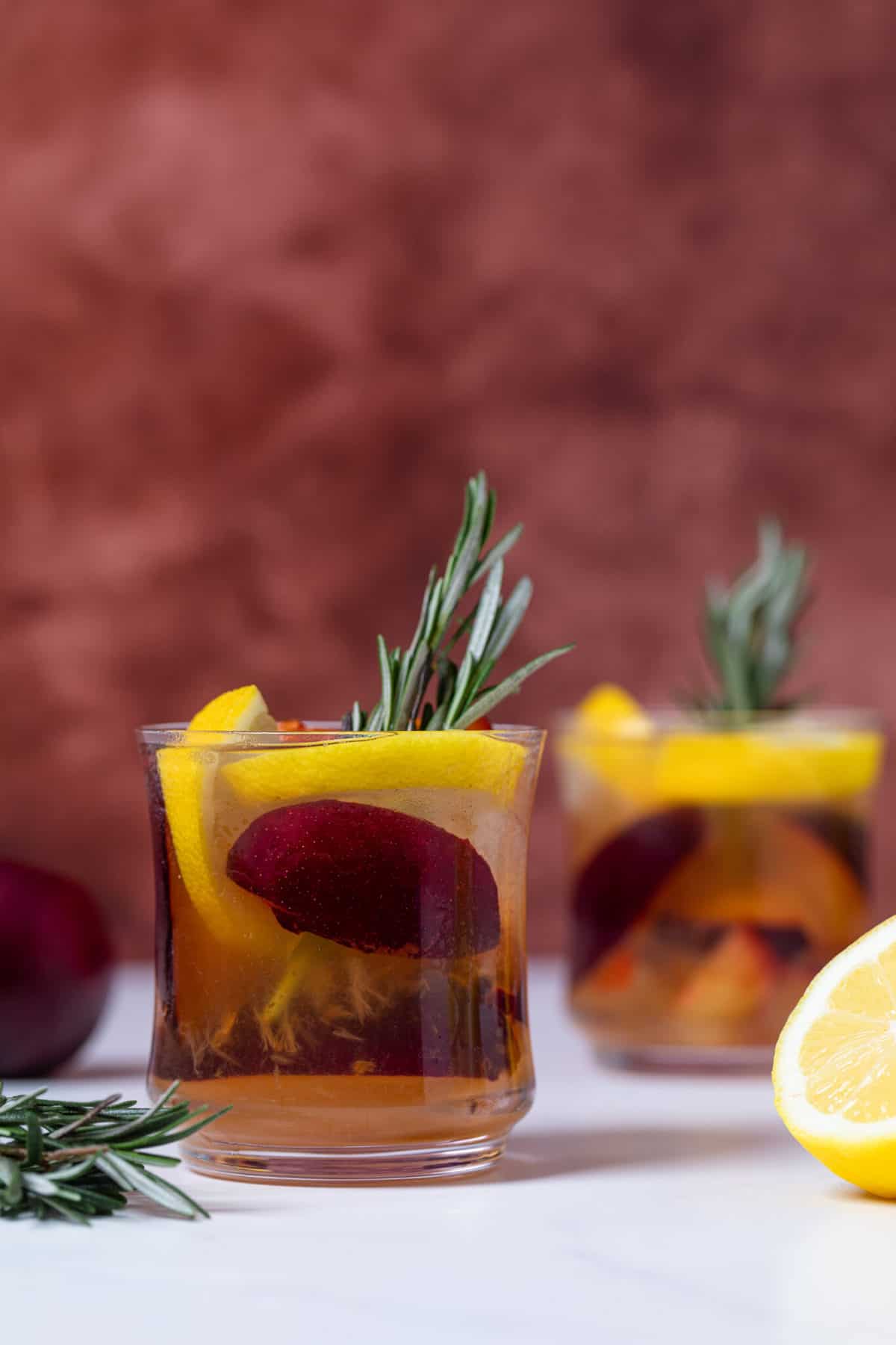  Plum Lemonade in a glass with rosemary and fresh fruit.