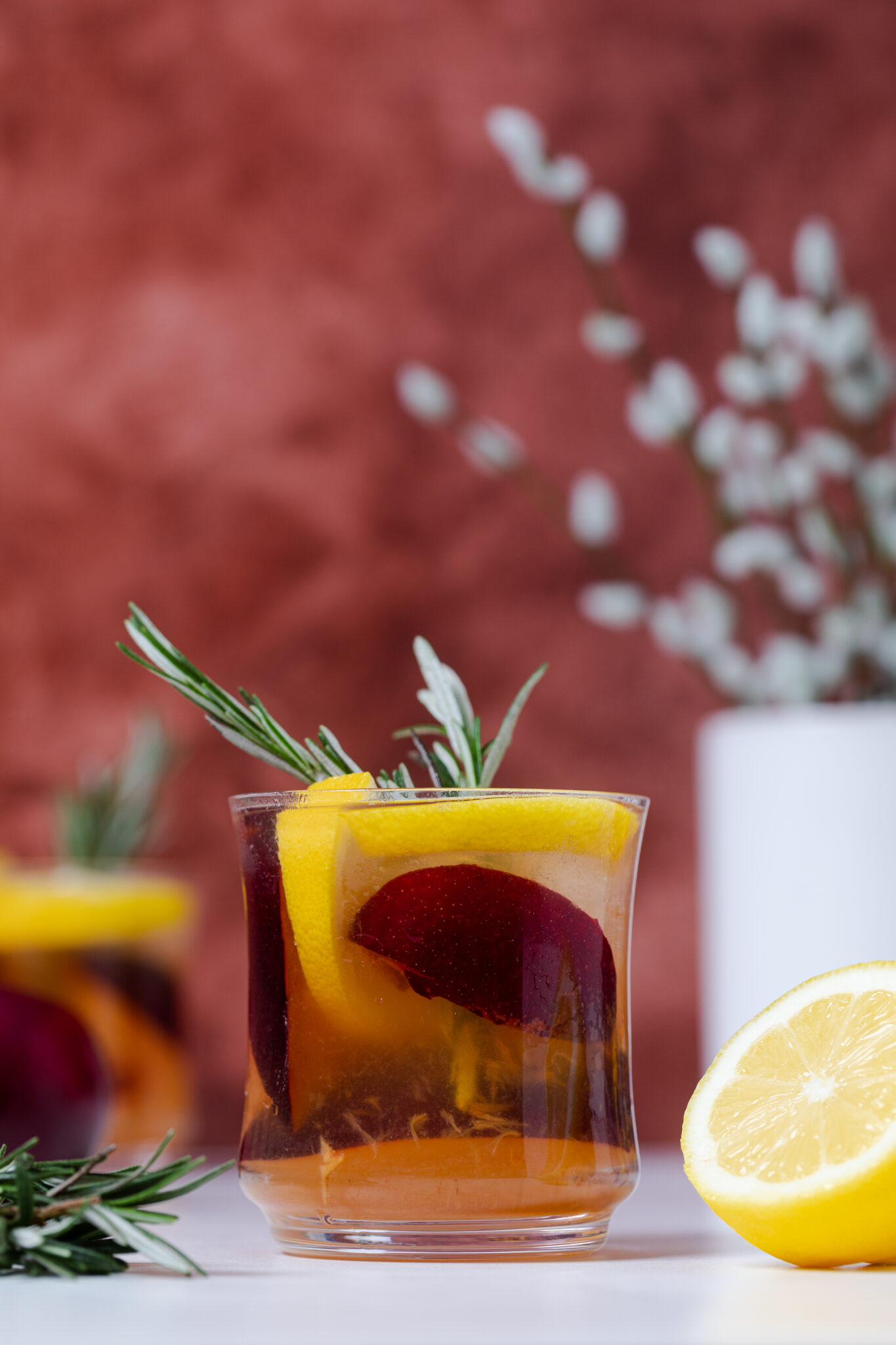  Plum Lemonade in a glass with rosemary and fresh fruit.