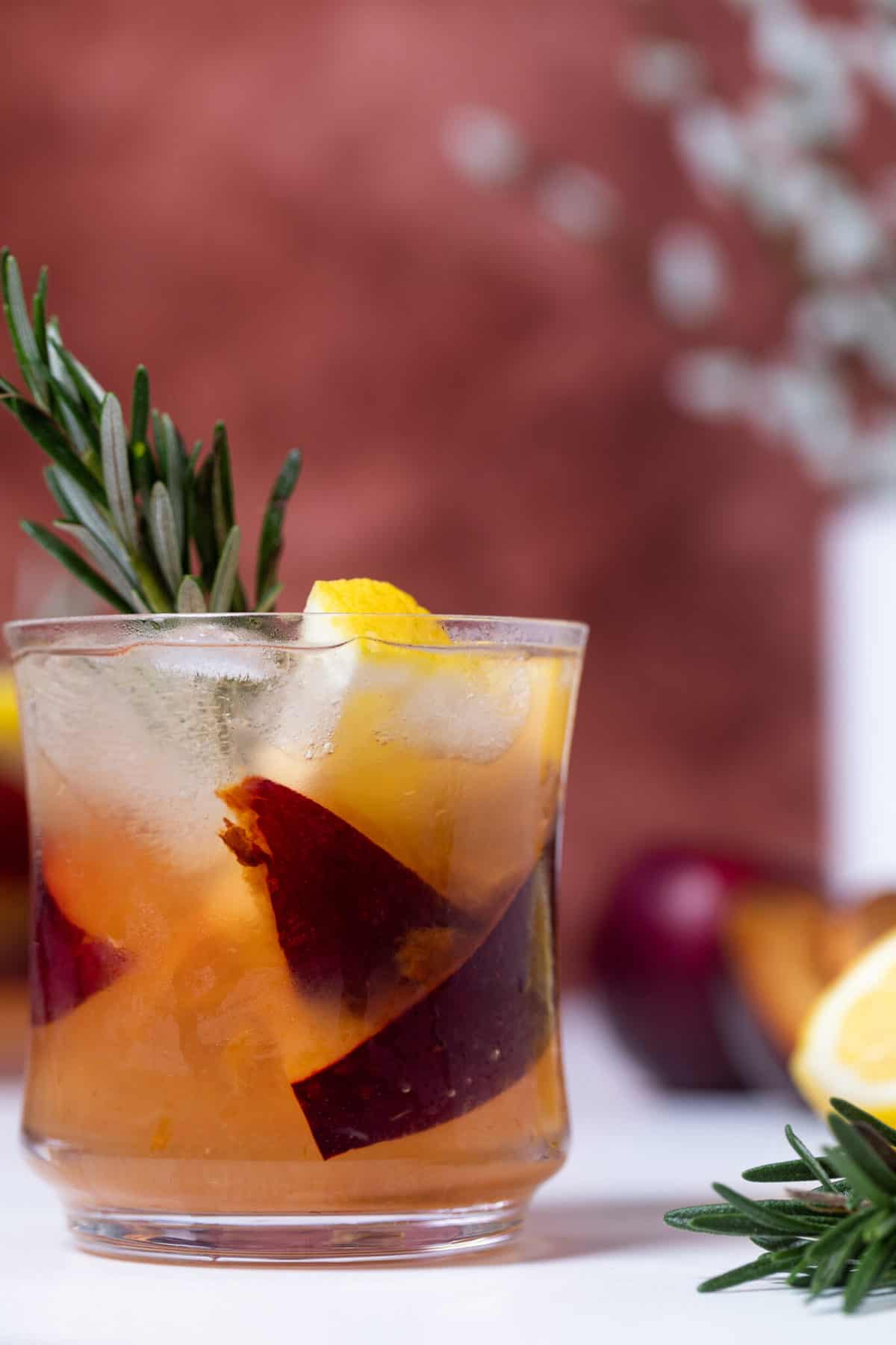  Plum Lemonade in a glass with fresh fruit and rosemary.