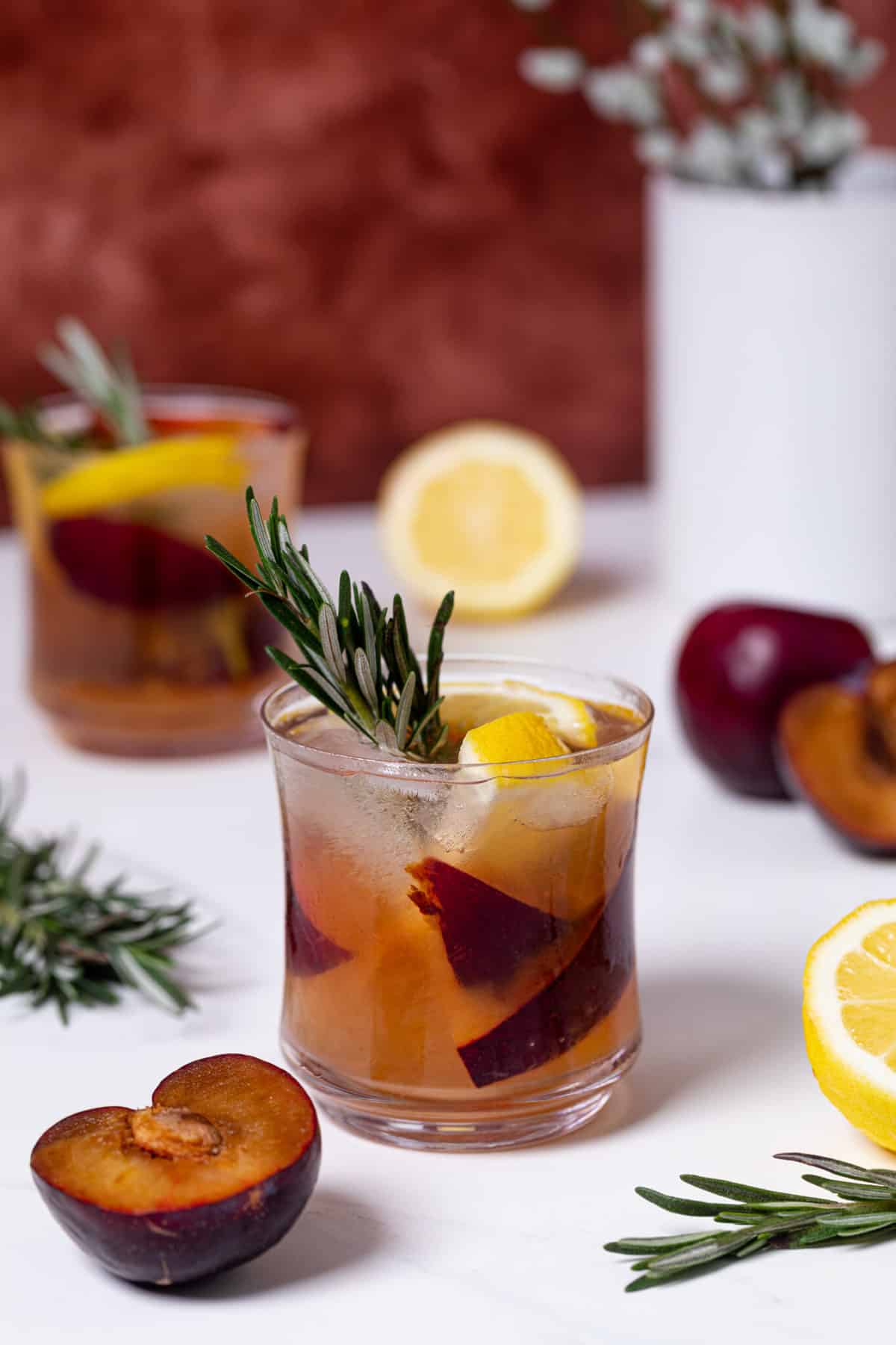 Plum Lemonade in a glass with rosemary and cut up fruit around.