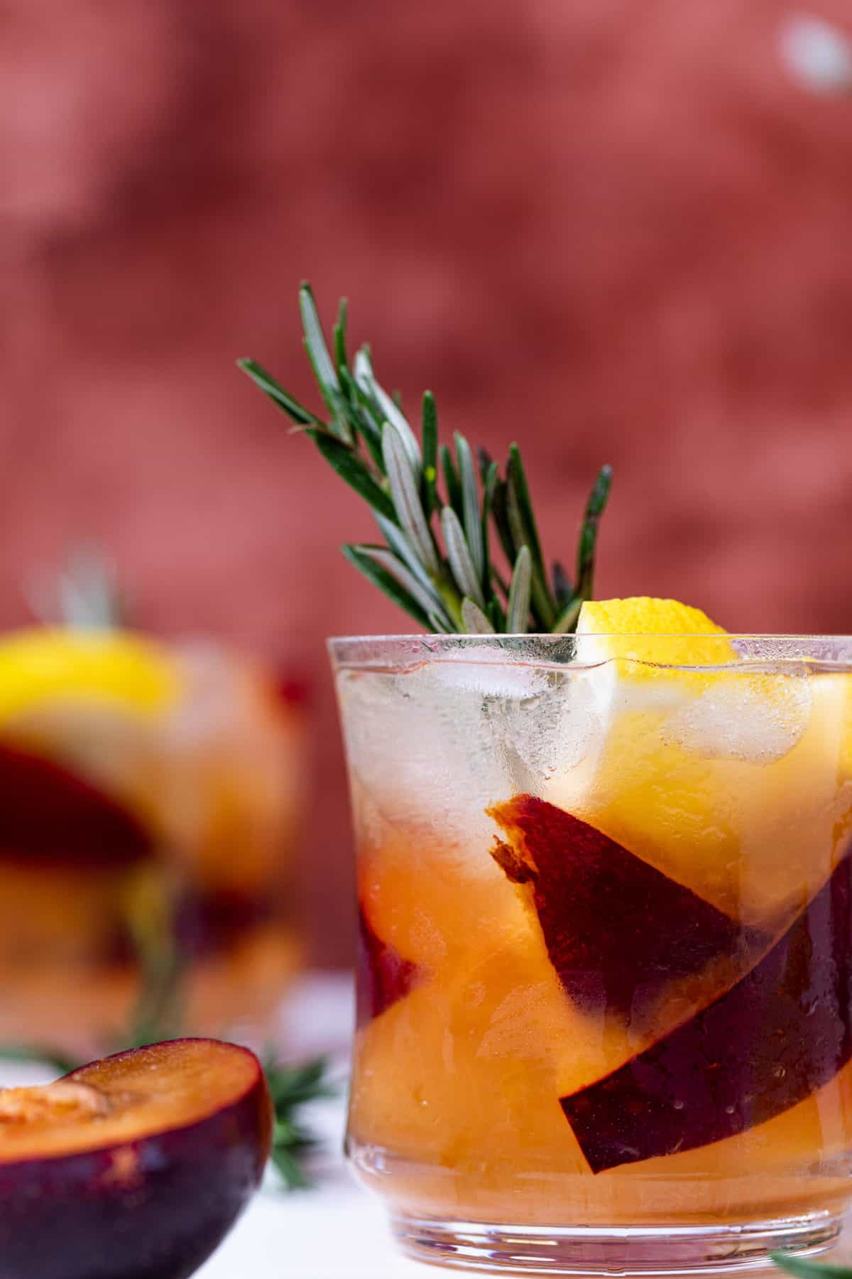 Glass of Plum Lemonade with fresh fruit and rosemary.