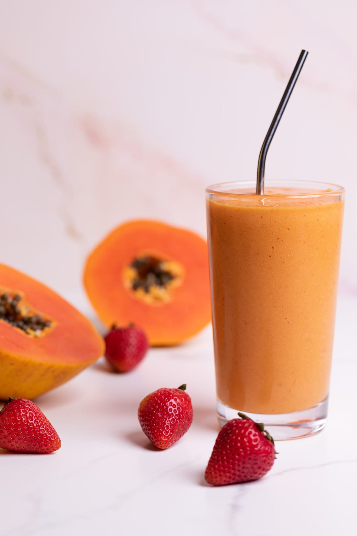 Strawberry Mango Papaya Smoothie in a glass with fresh berries and papaya on the side