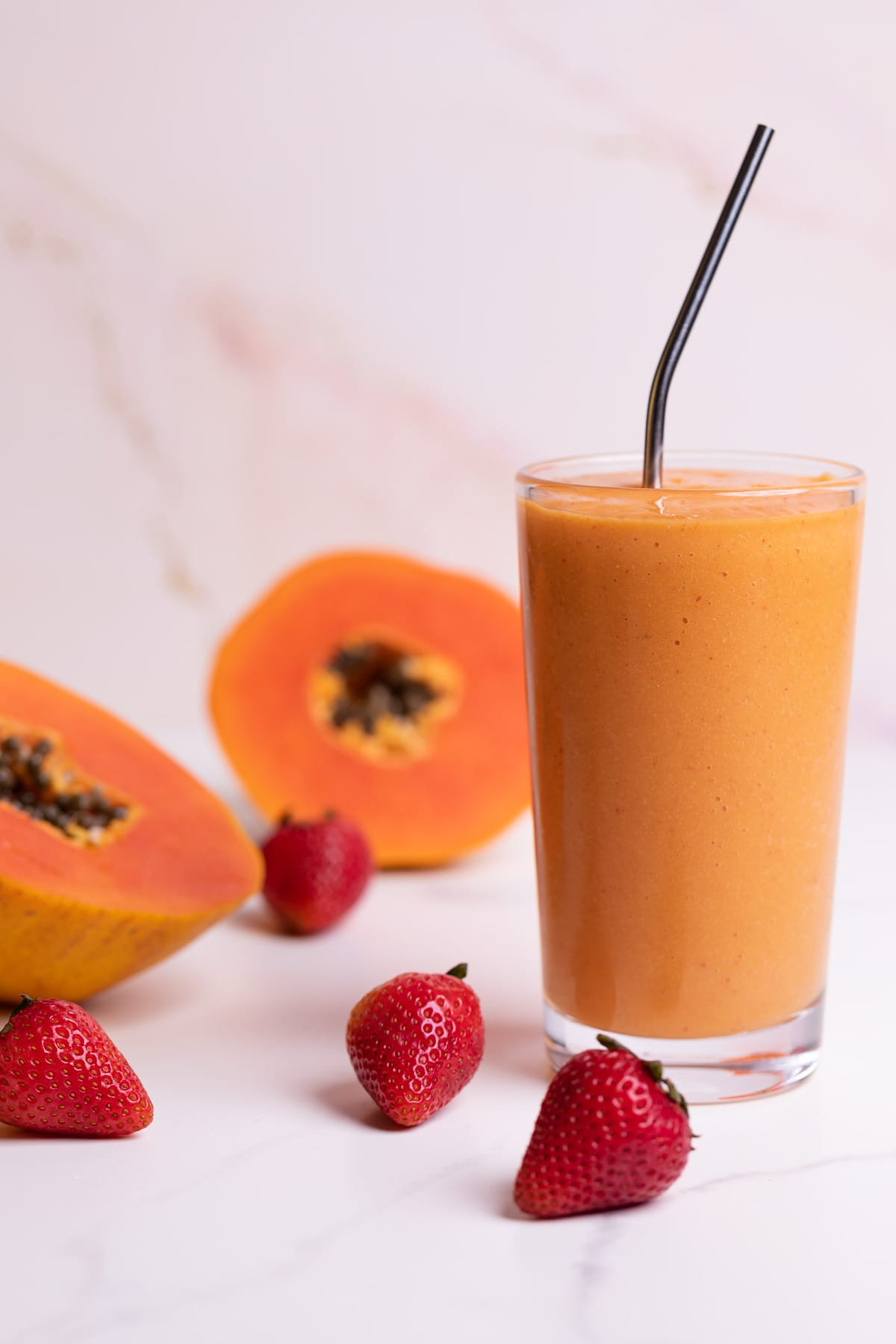 Strawberry Mango Papaya Smoothie in a glass with fresh berries and papaya on the side.