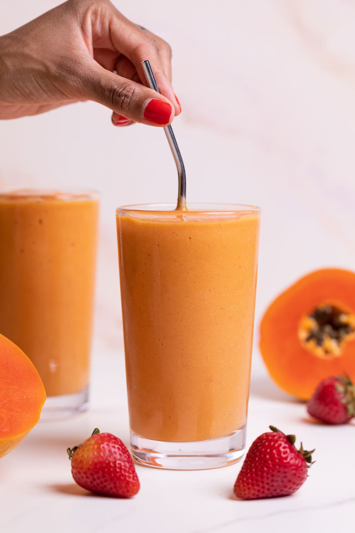 Person stirring a Strawberry Mango Papaya Smoothie with a metal straw.