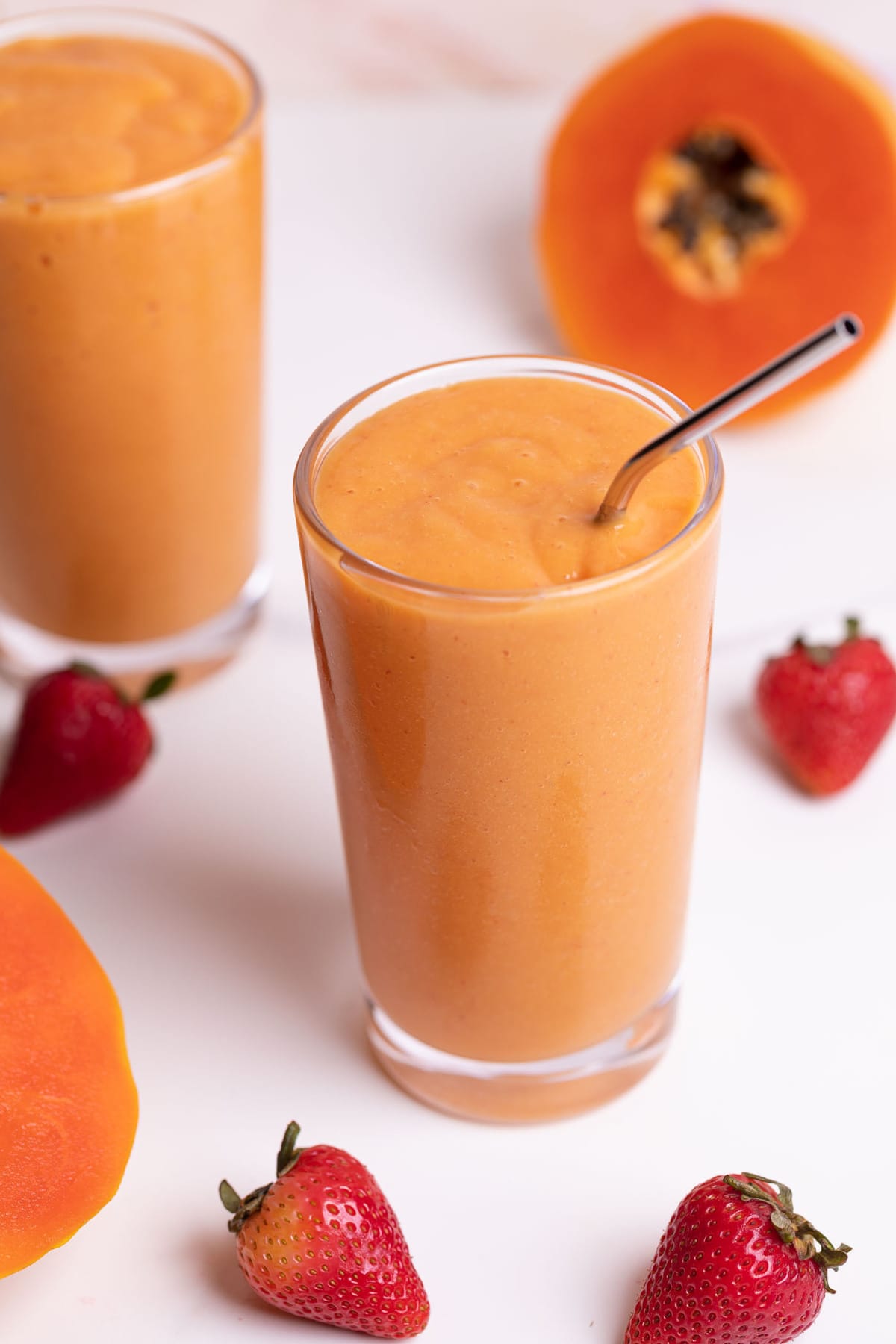 Two glasses of papaya smoothies with fresh strawberries on the side.