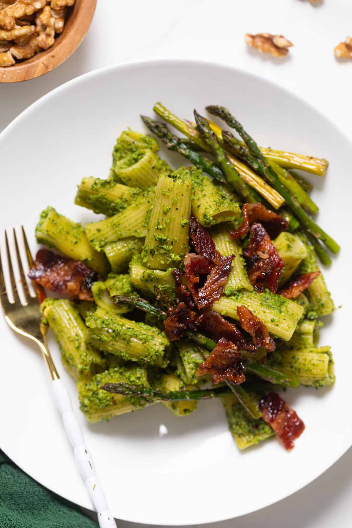 Pesto Pasta with Asparagus + Bacon on a white plate with a gold and white fork