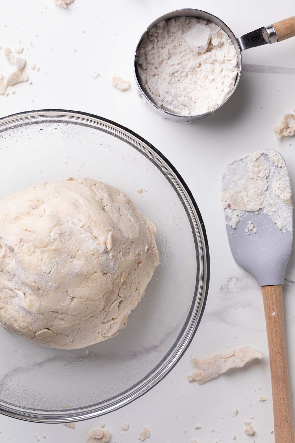 Easy Homemade Gluten-Free Pizza Crust in a glass bowl with a measuring cup and a spatula on the side.