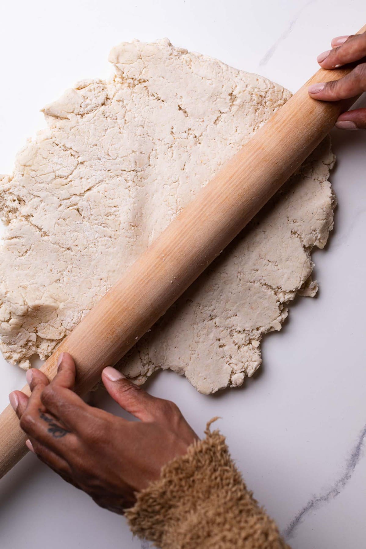 Homemade Gluten-Free Pizza Crust dough being rolled out by a wooden rolling pin.