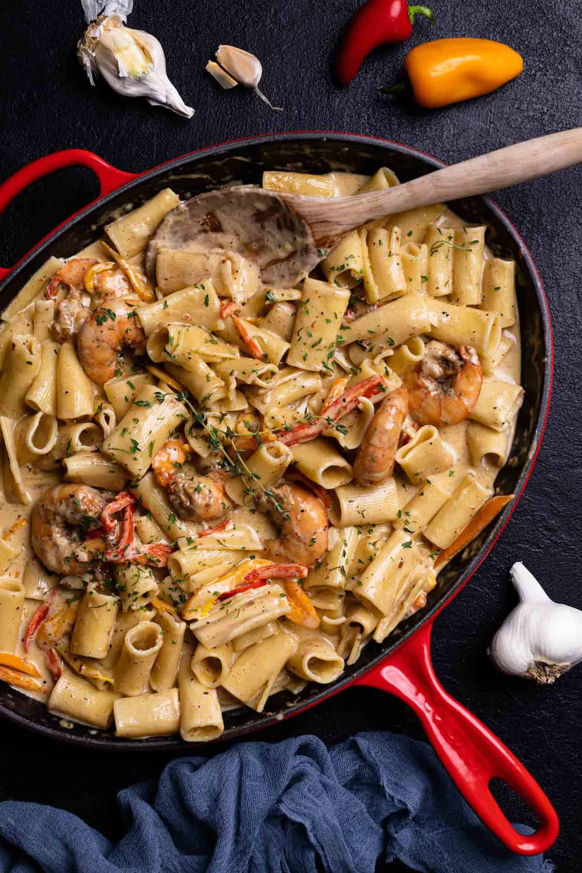 Creamy Jamaican Shrimp Pasta in a skillet with a wooden spoon and fresh thyme
