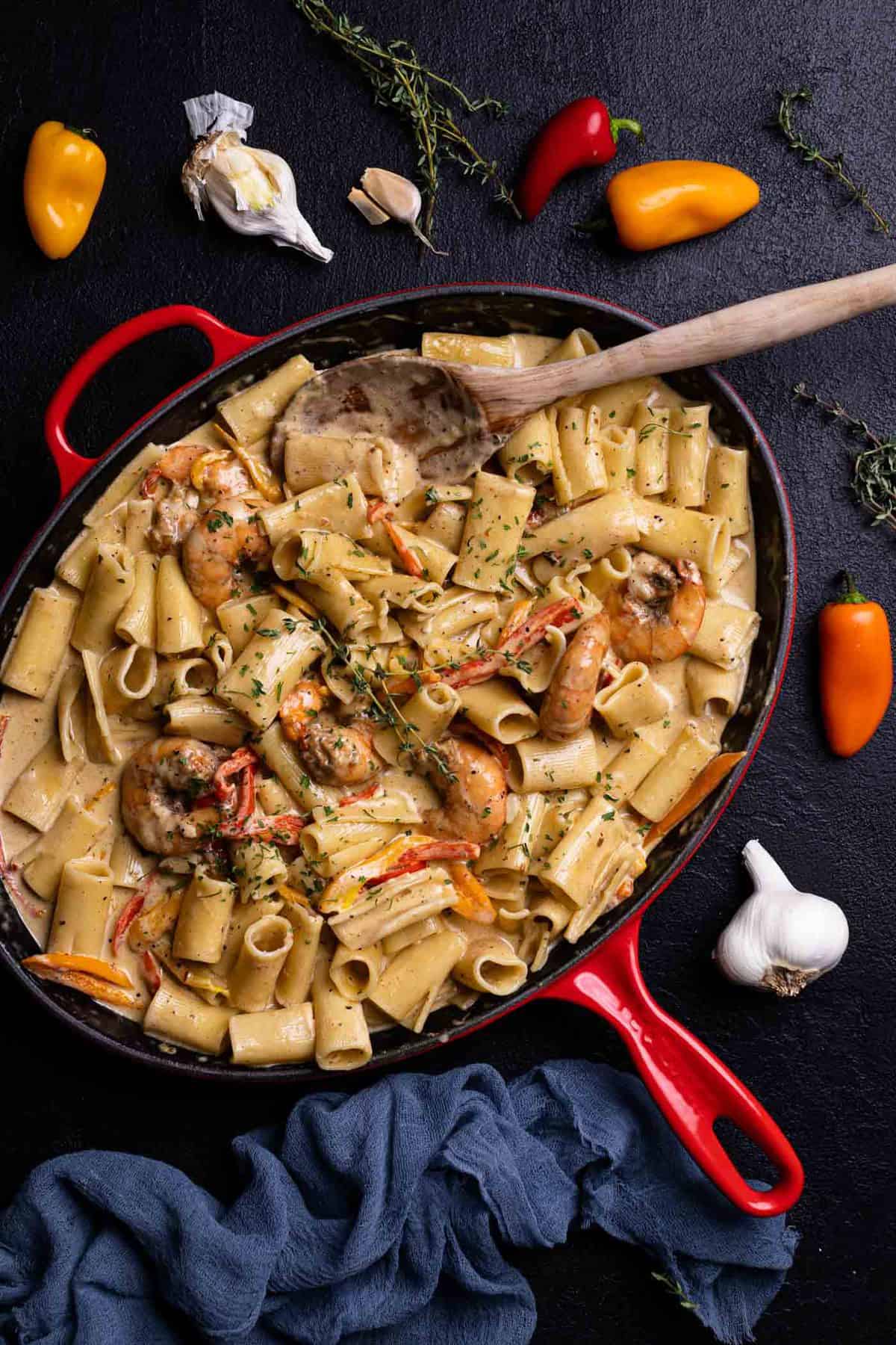 Creamy Jamaican Shrimp Pasta in a skillet with a wooden spoon and fresh thyme.