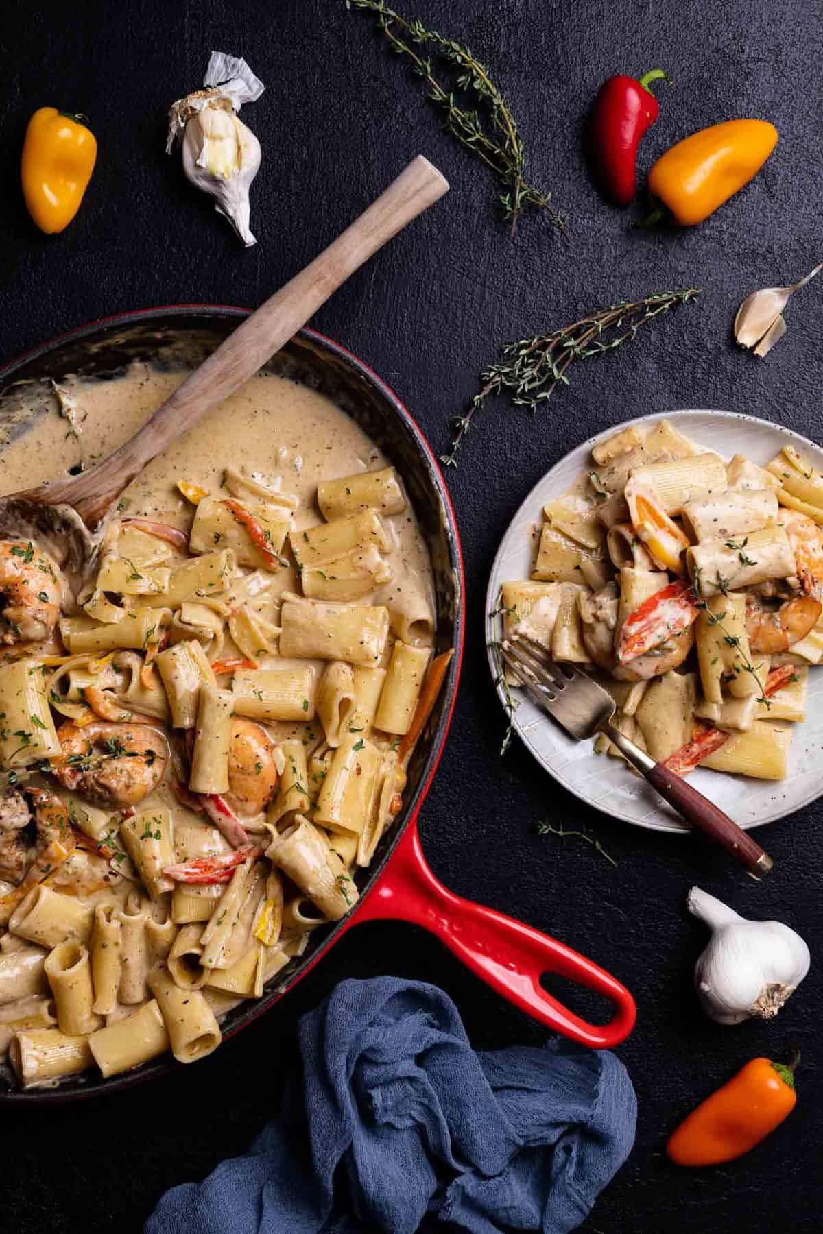 Creamy Jamaican Shrimp Pasta in a skillet with a wooden spoon and fresh thyme and a plate of pasta on the side