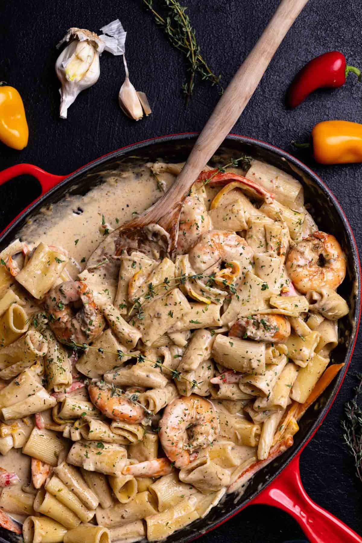 Creamy Jamaican Shrimp Pasta in a red skillet with a wooden spoon and fresh thyme.