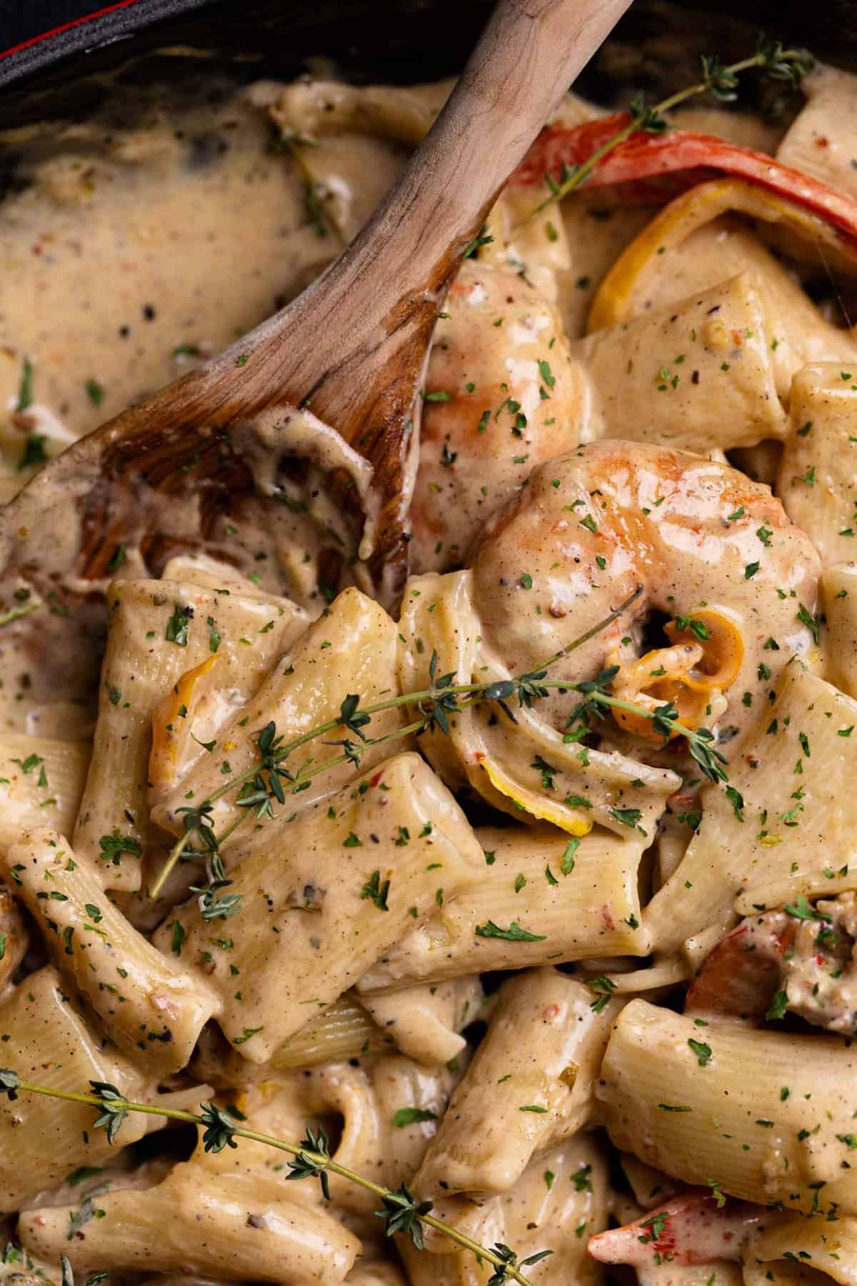 Creamy Jamaican Shrimp Pasta in a skillet with a wooden spoon and fresh thyme