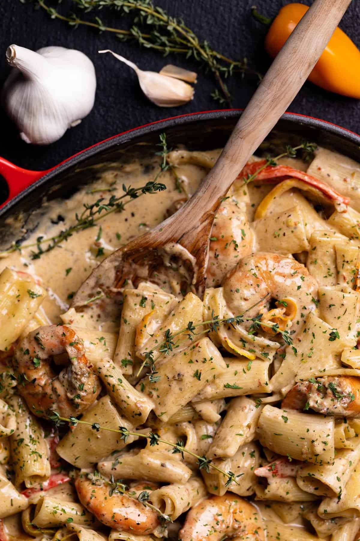 Creamy Jamaican Shrimp Pasta in a red skillet with a wooden spoon and fresh thyme.