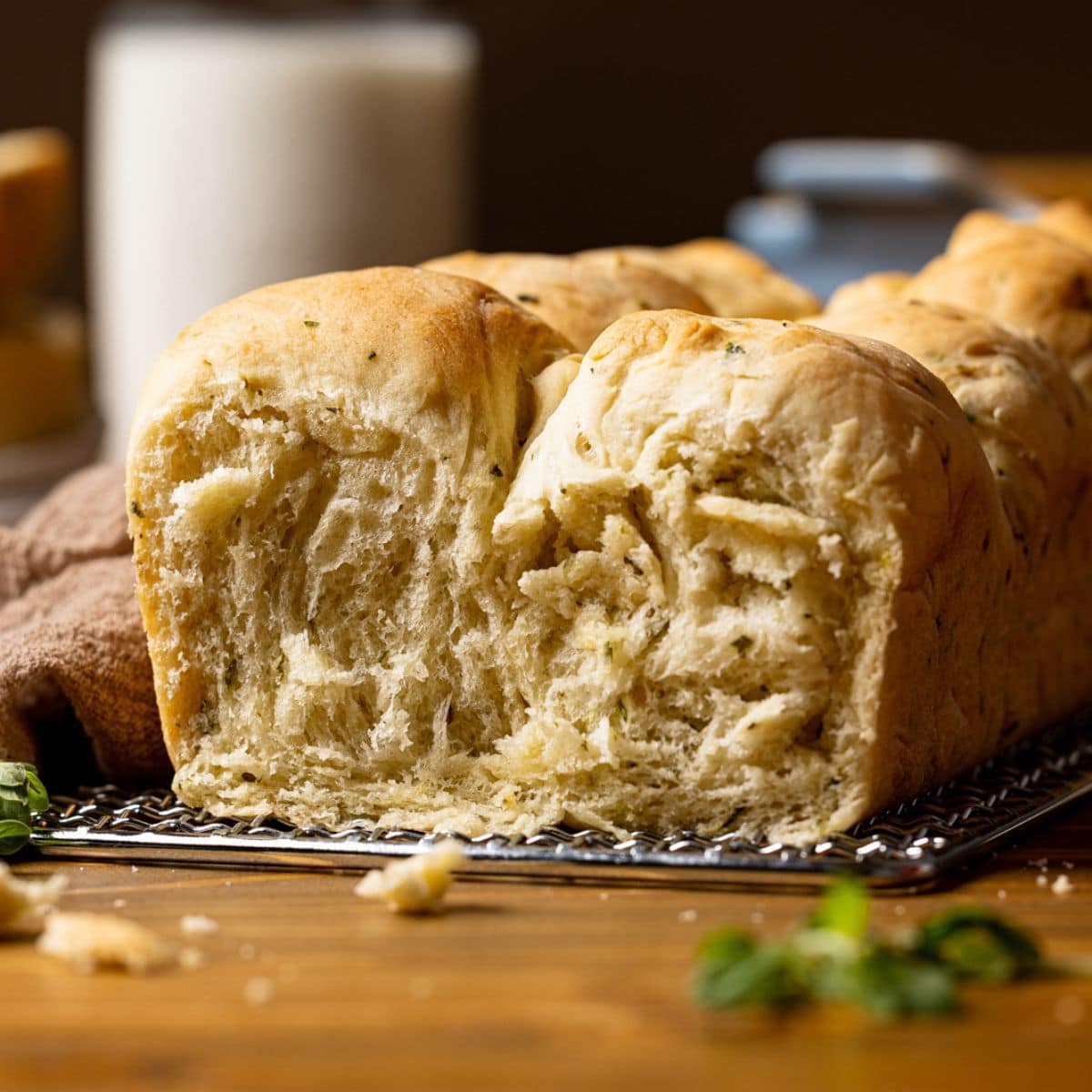 Up close shot of baked bread with a slice removed on a brown table with a cup of milk in the background.