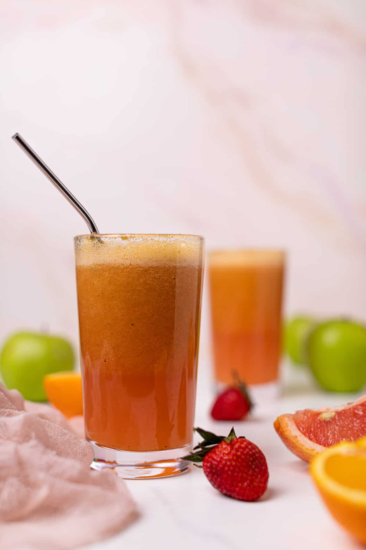 Apple Citrus Strawberry Juice in two glasses with a metal straw and fresh fruit.