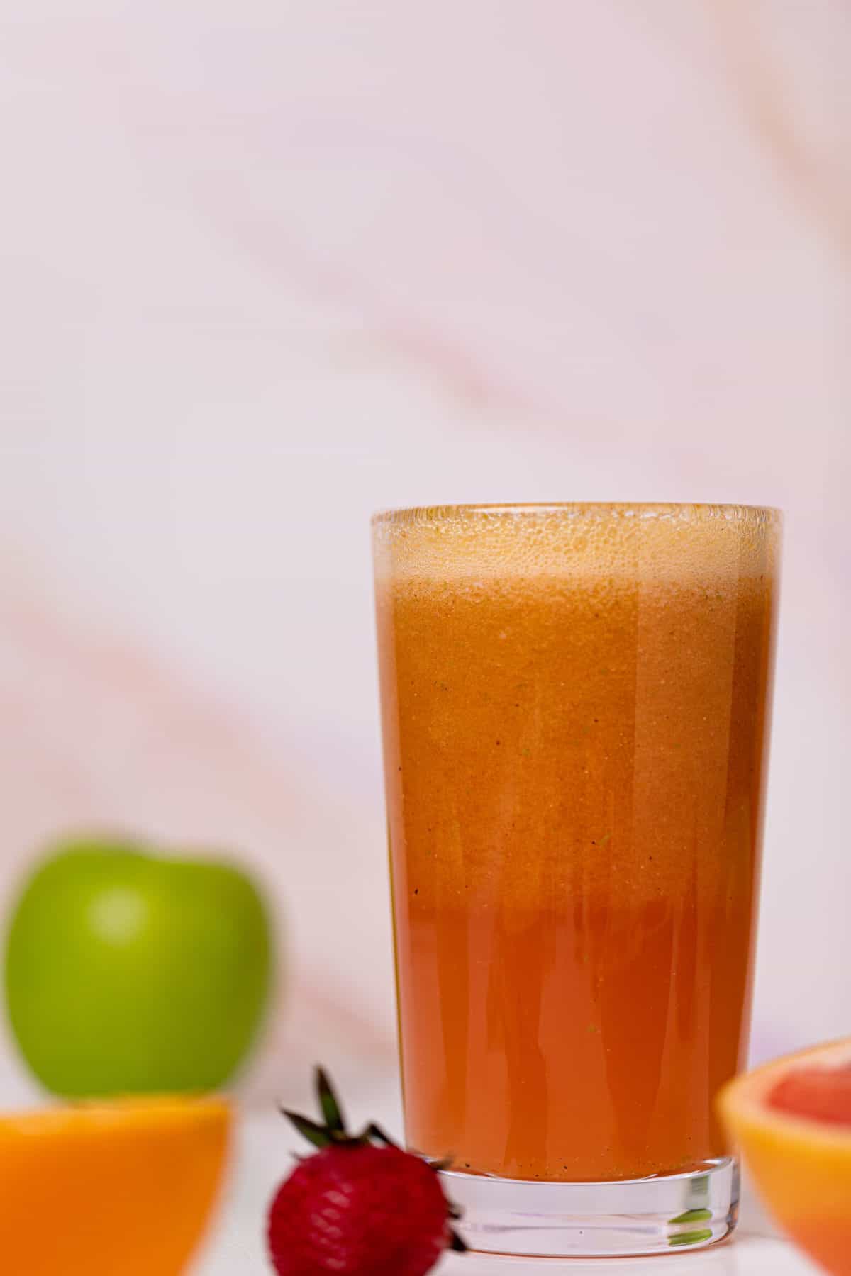 Apple Citrus Strawberry Juice in a glass with fresh fruit on the side.