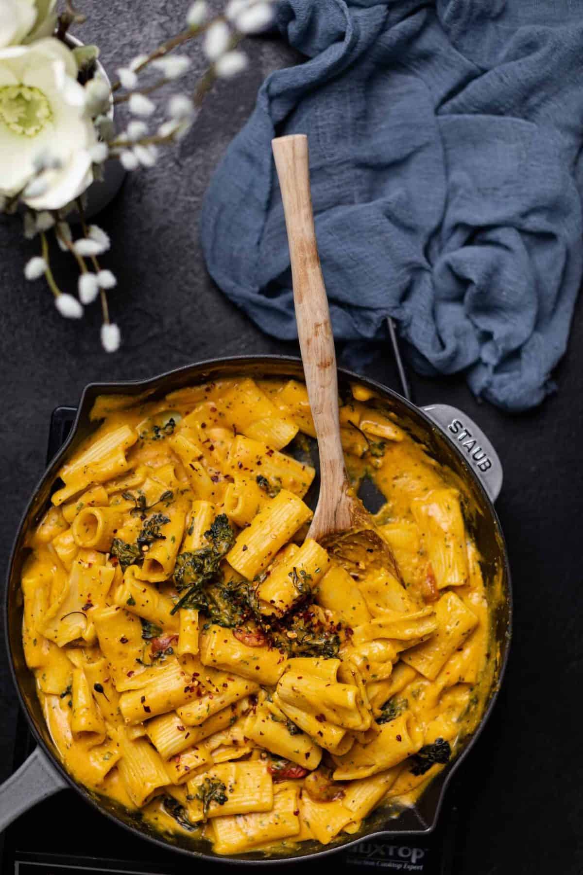 Vegan sweet potato pasta skillet with roasted broccolini in a cast iron pan with a wooden spoon