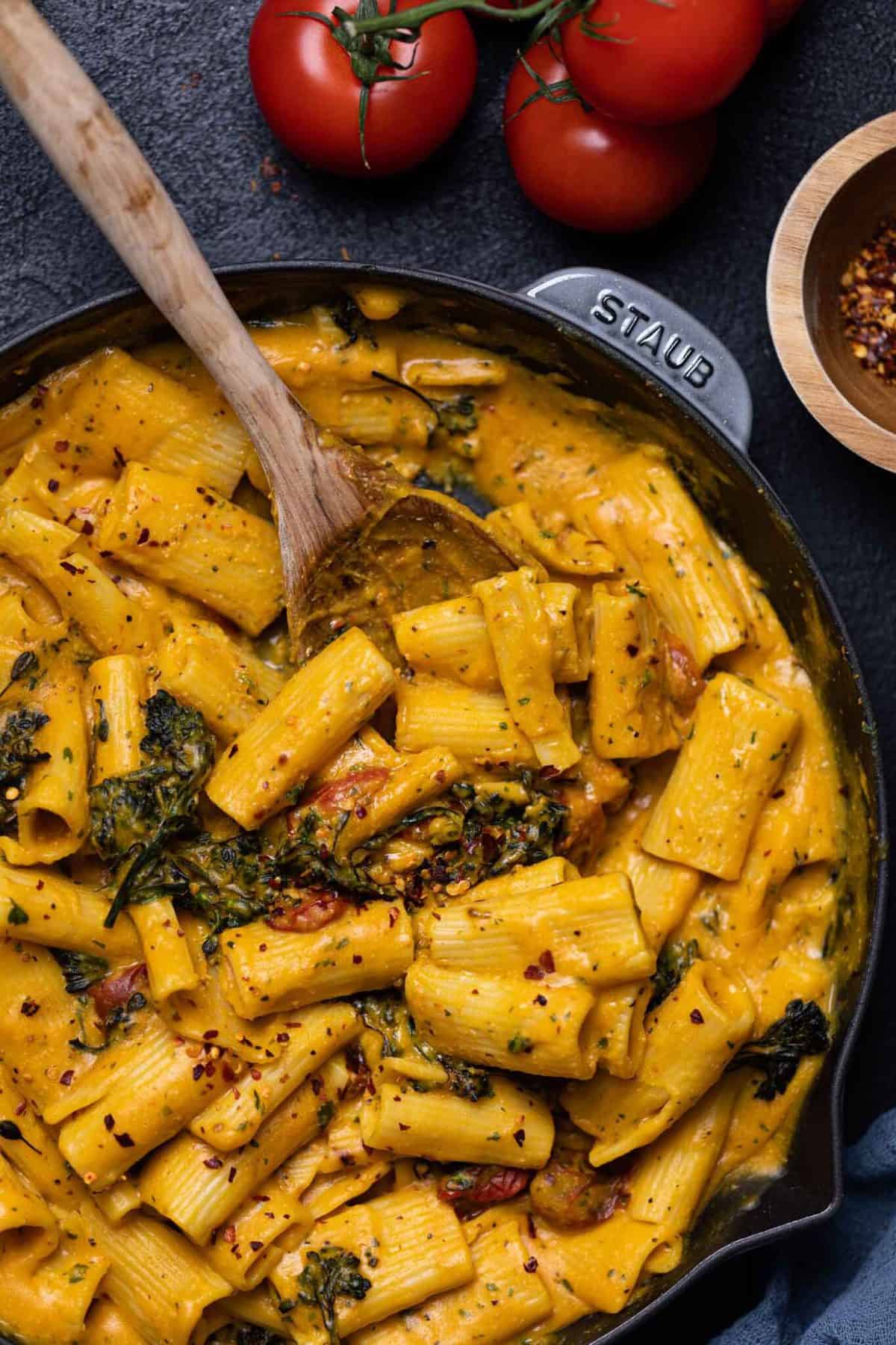 Wooden spoon stirring a skillet of Creamy Vegan Sweet Potato Rigatoni Pasta