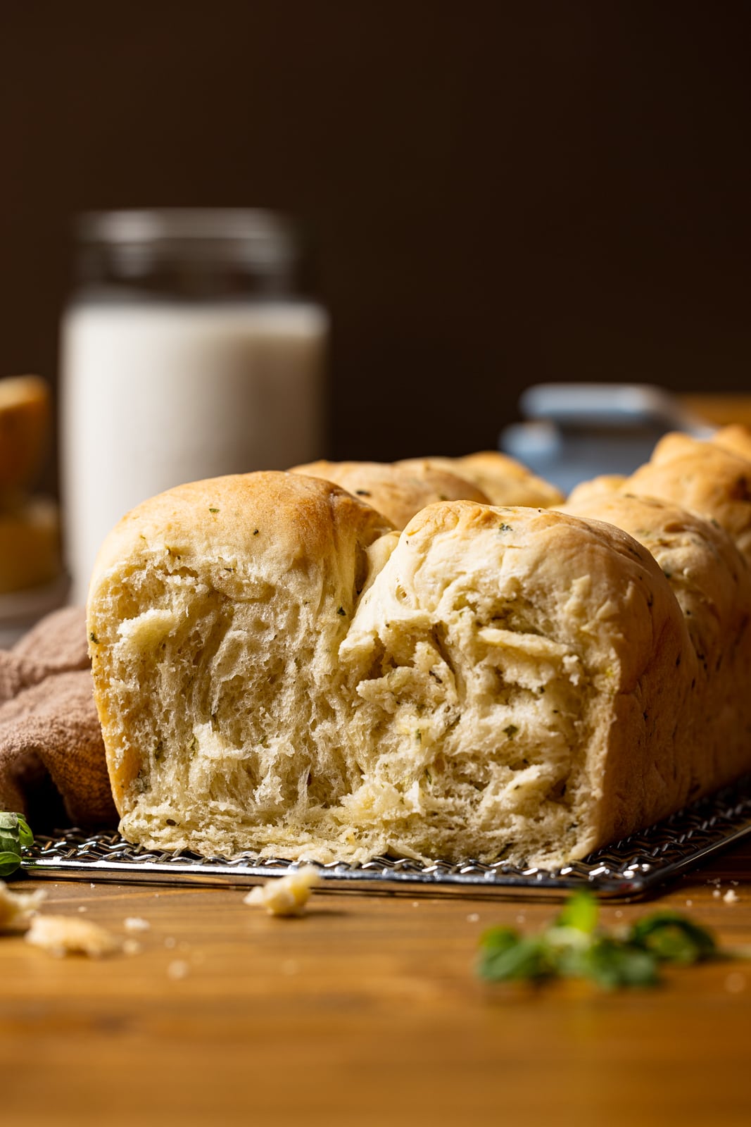 Up close shot of baked bread with a slice removed on a brown table with a cup of milk in the background.