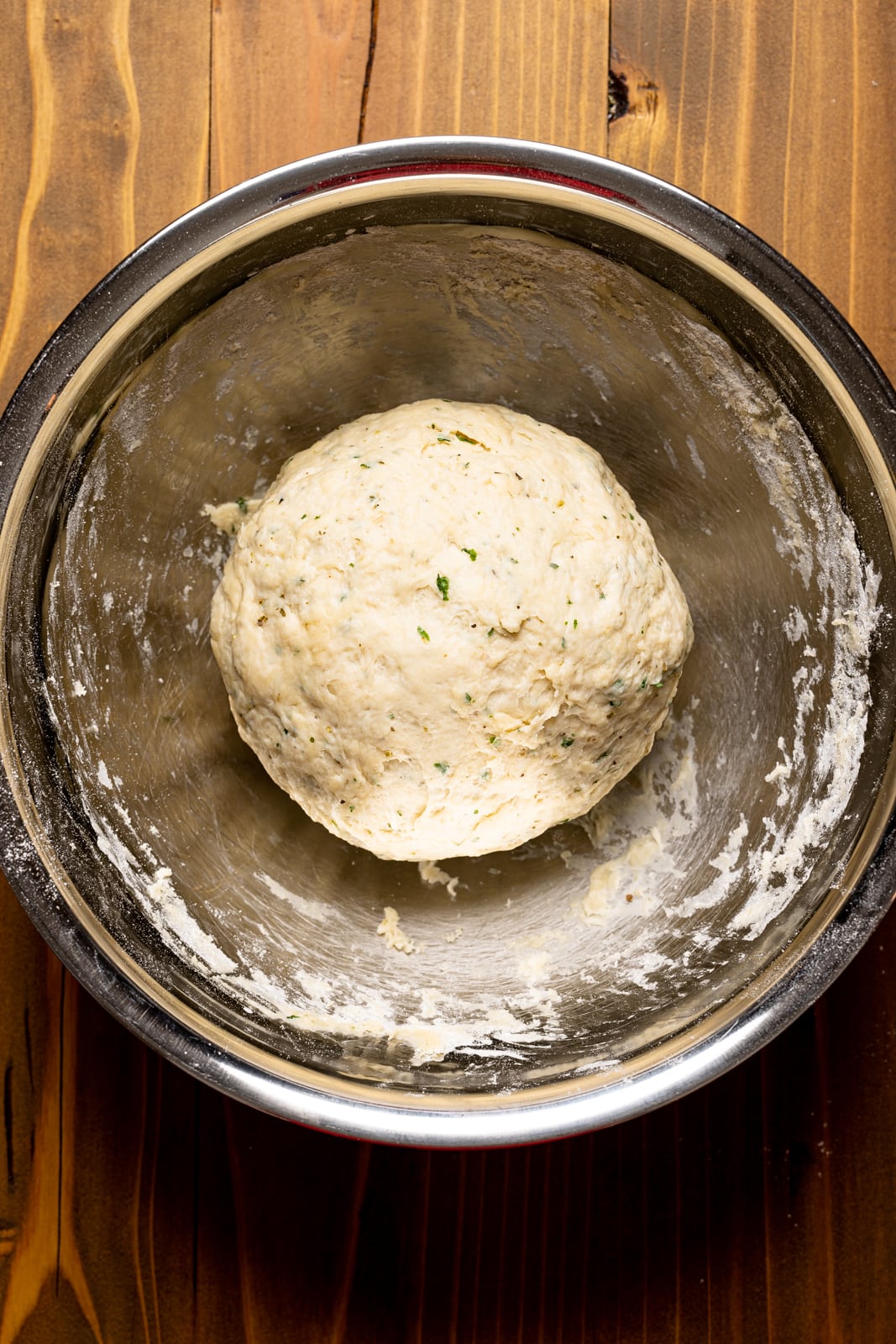 Dough in a large silver bowl on a brown wood table.