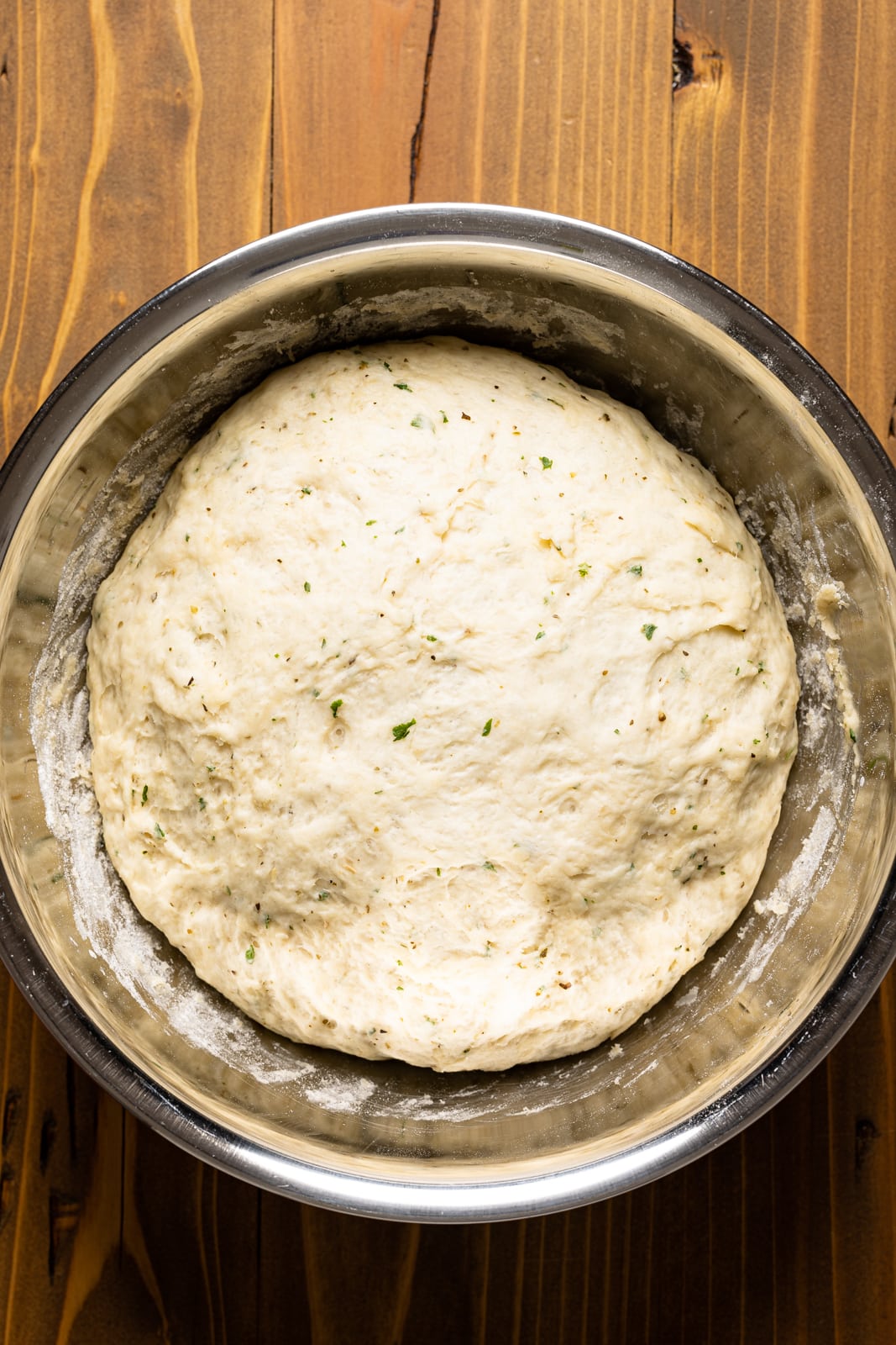 Risen dough in a large silver bowl on a brown wood table.