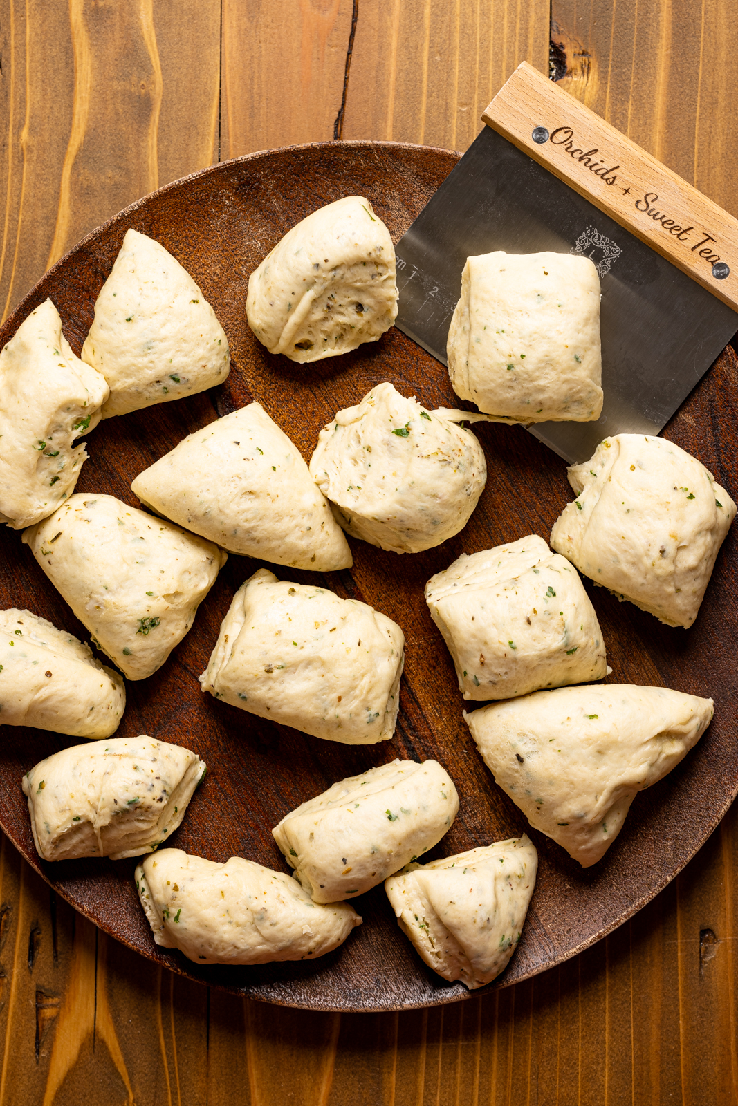 Dough cut into pieces using a pastry blender on a wood plate on a wood table.