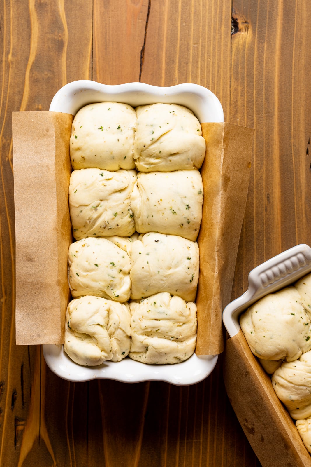 Dough in a bread pan line with parchment paper on a brown wood table.