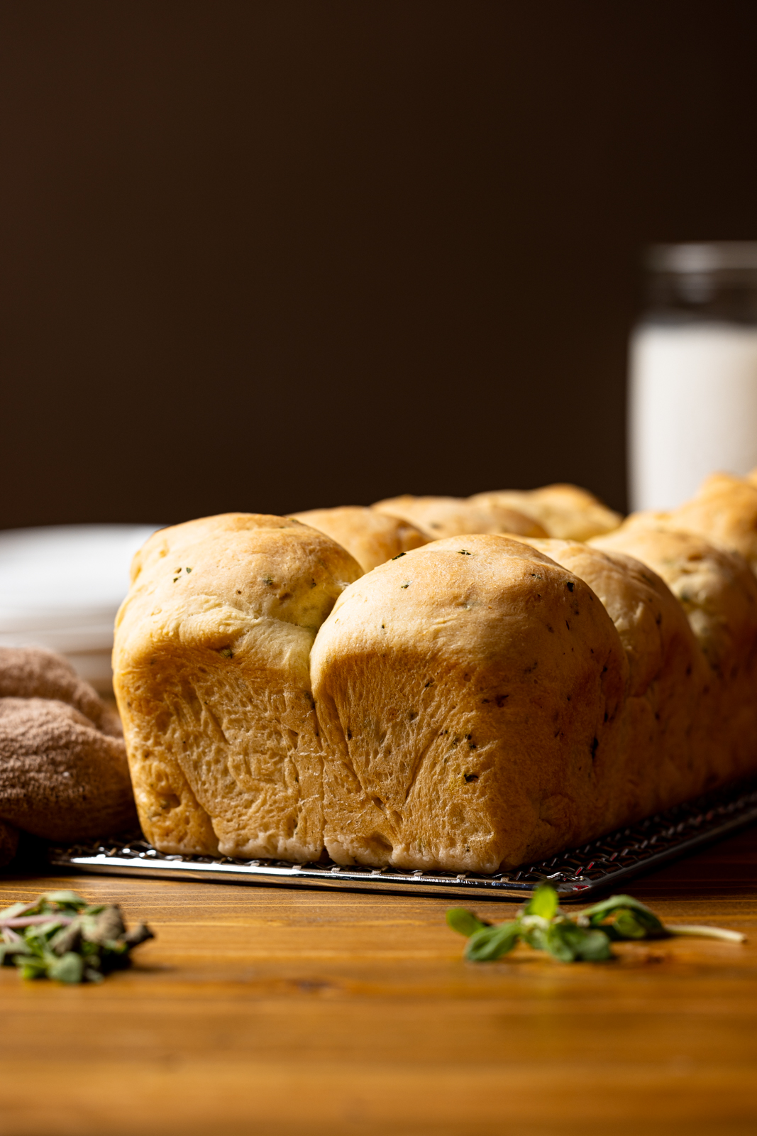 Front view of baked bread on a silver tray on a brown wood table with a brown napkin and jar of milk in the background.