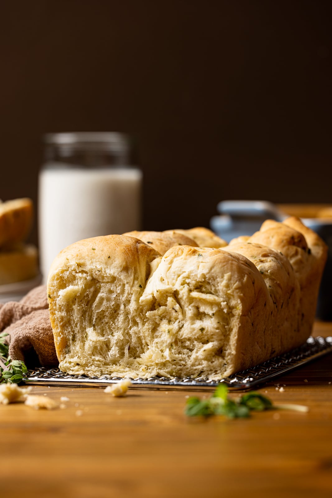 Baked bread with a slice removed on a silver tray on a brown wood table with a jar of milk in the background and brown napkin.