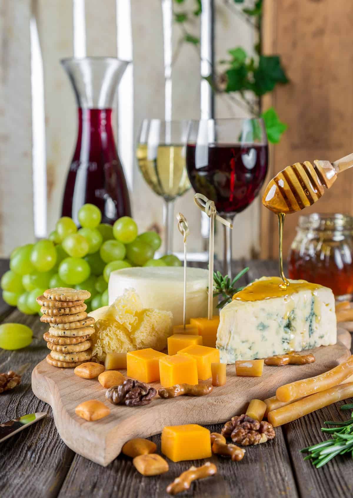 Board with cheese, crackers, honey, and glasses of wine.