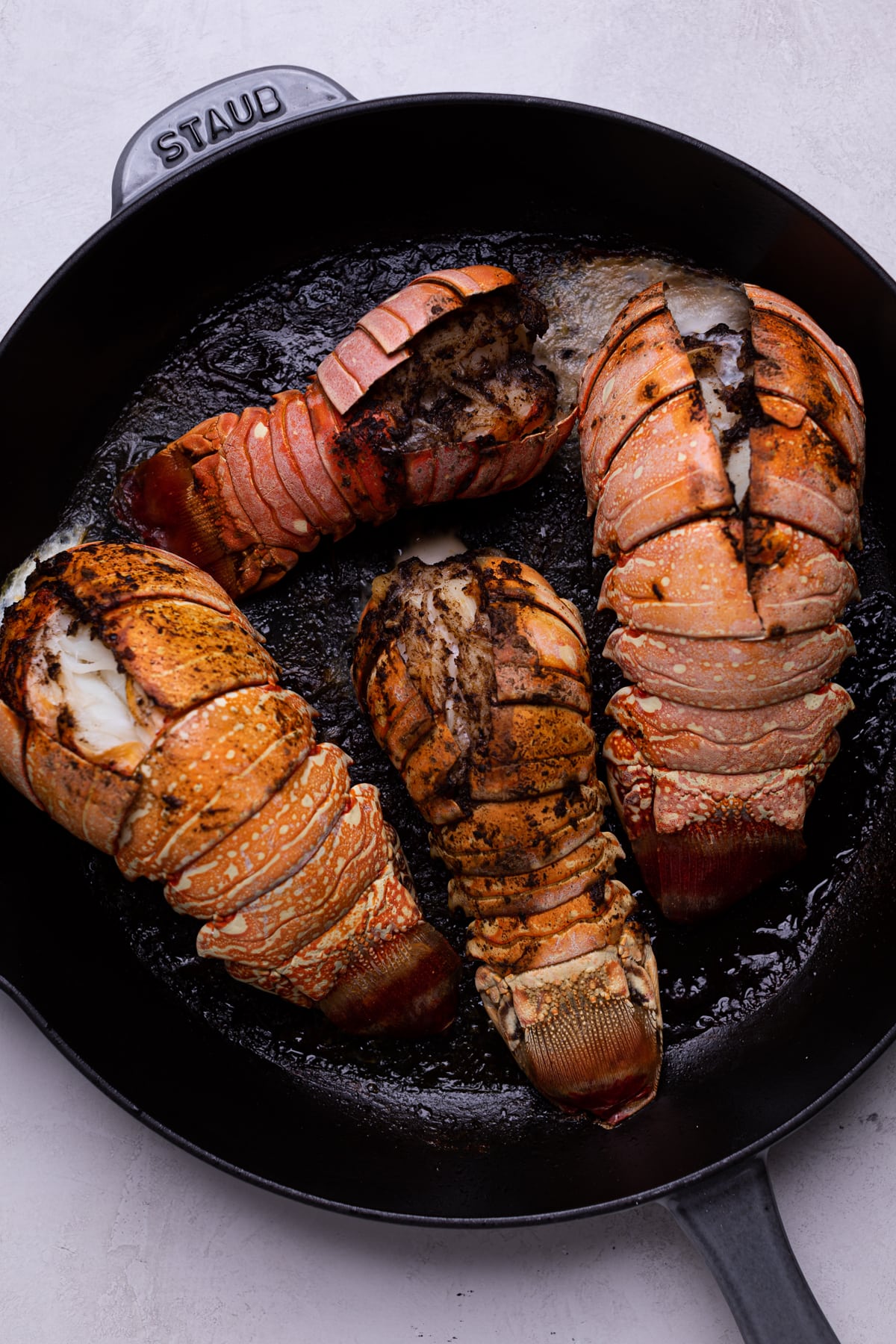 Cast iron skillet with four lobster tails cooking.