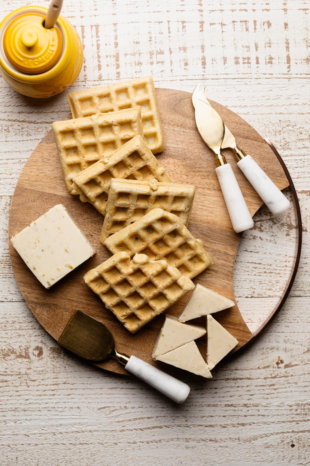 Waffles on a wooden board with vegan cheese and cheese slicers.