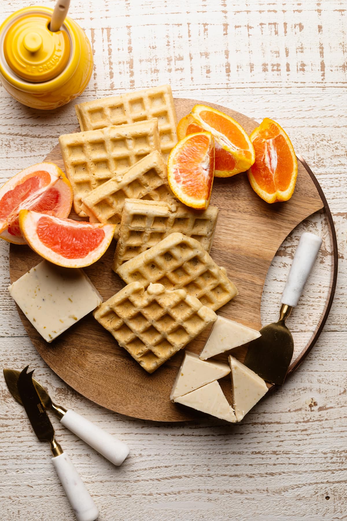 Vegan cheese, waffles, and citrus fruits on a wooden board.