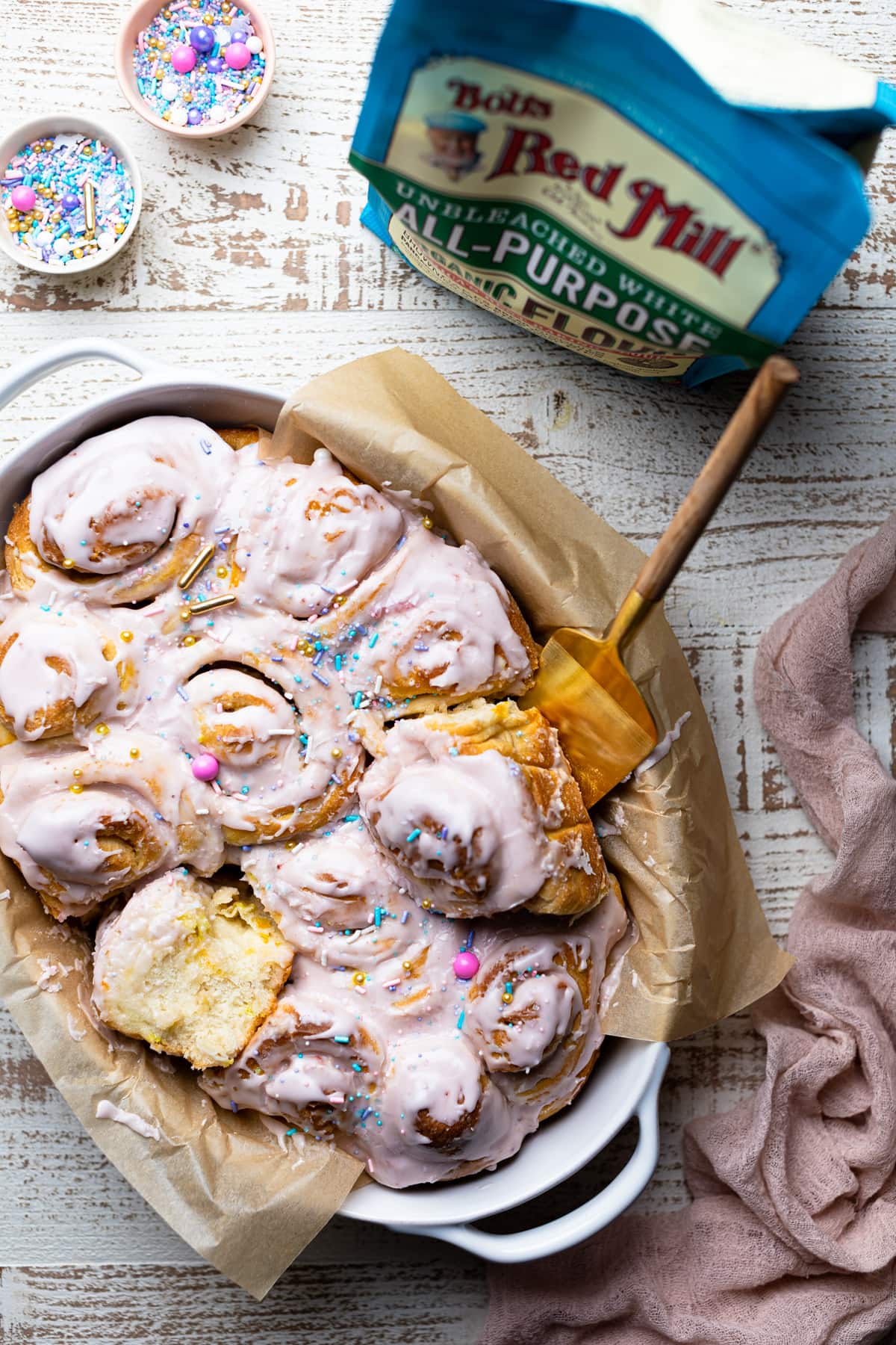 White pan of Vegan Funfetti Cinnamon Rolls with a golden spatula.