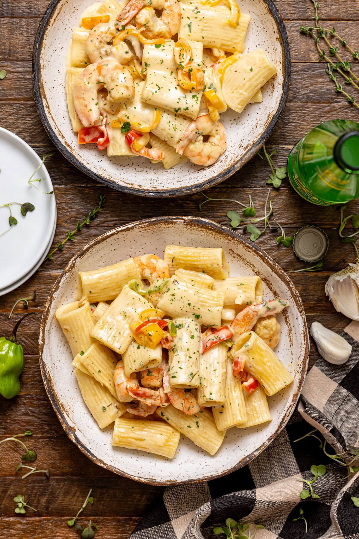 Two bowls of rasta pasta with a drink on a brown wood table.