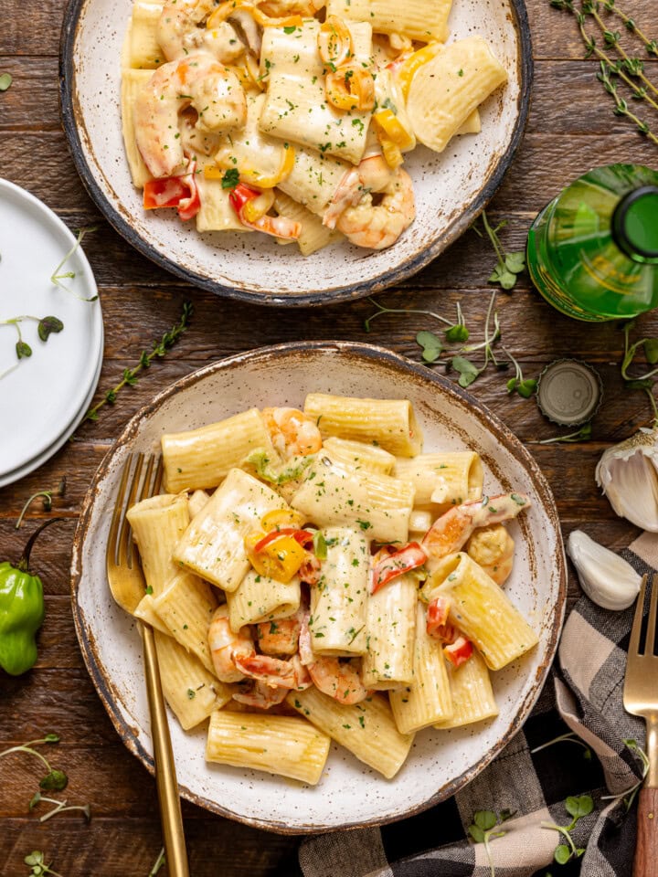 Two bowls of rasta pasta with forks and a drink on a brown wood table.