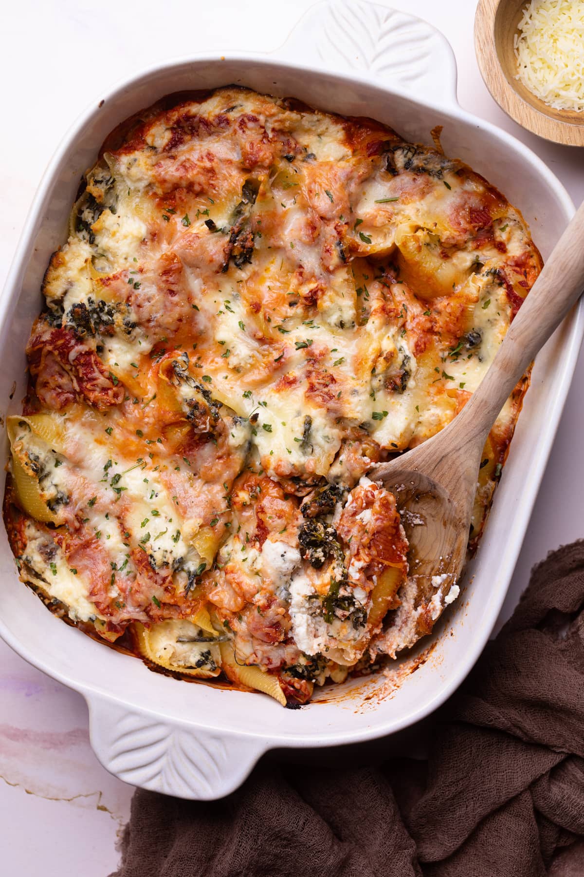 White dish of Roasted Broccolini and Chicken Ricotta Stuffed Shells with a wooden spoon.