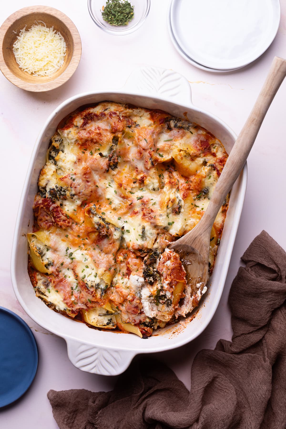 White, handled dish of Roasted Broccolini and Chicken Ricotta Stuffed Shells with a wooden spoon.