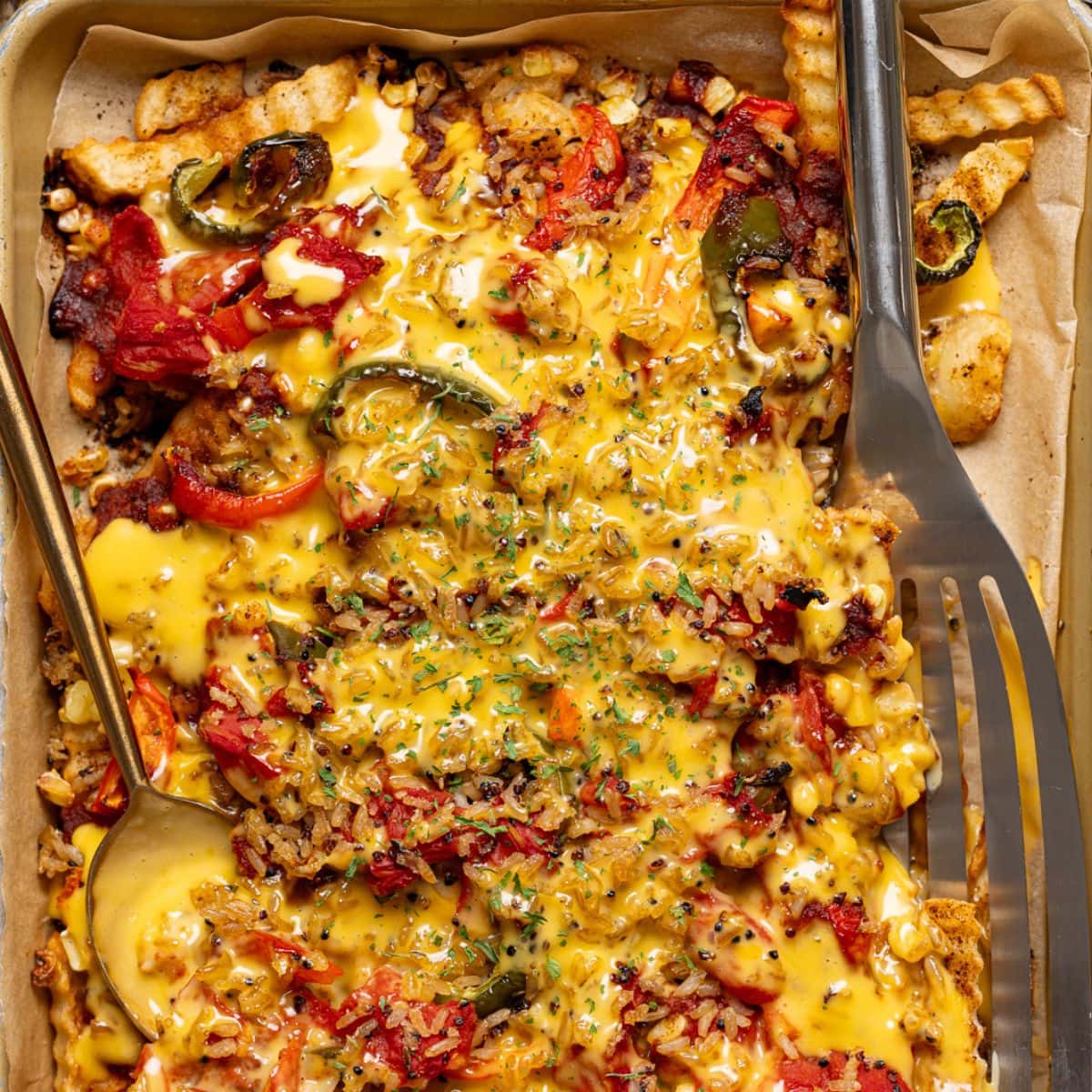 Nacho fries in a sheet pan with spatula and spoon with a side of ketchup.