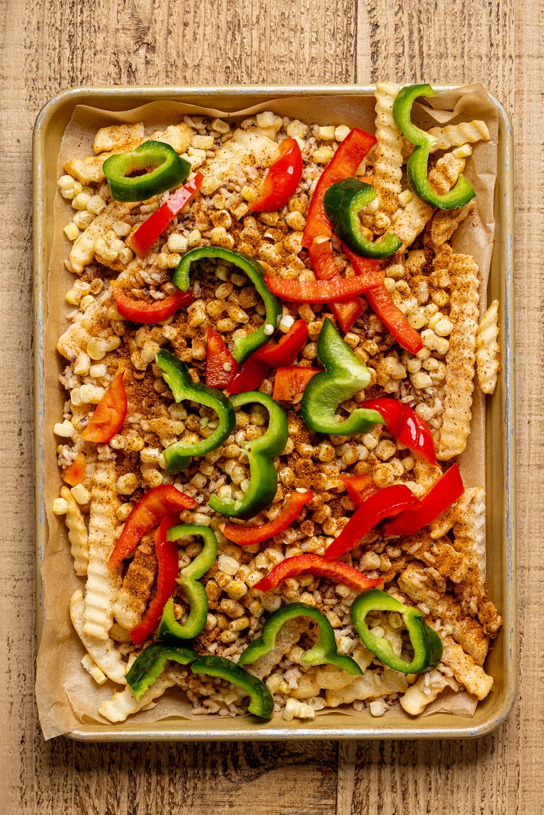 Fries on sheet pan with corn, quinoa, and peppers as topping.