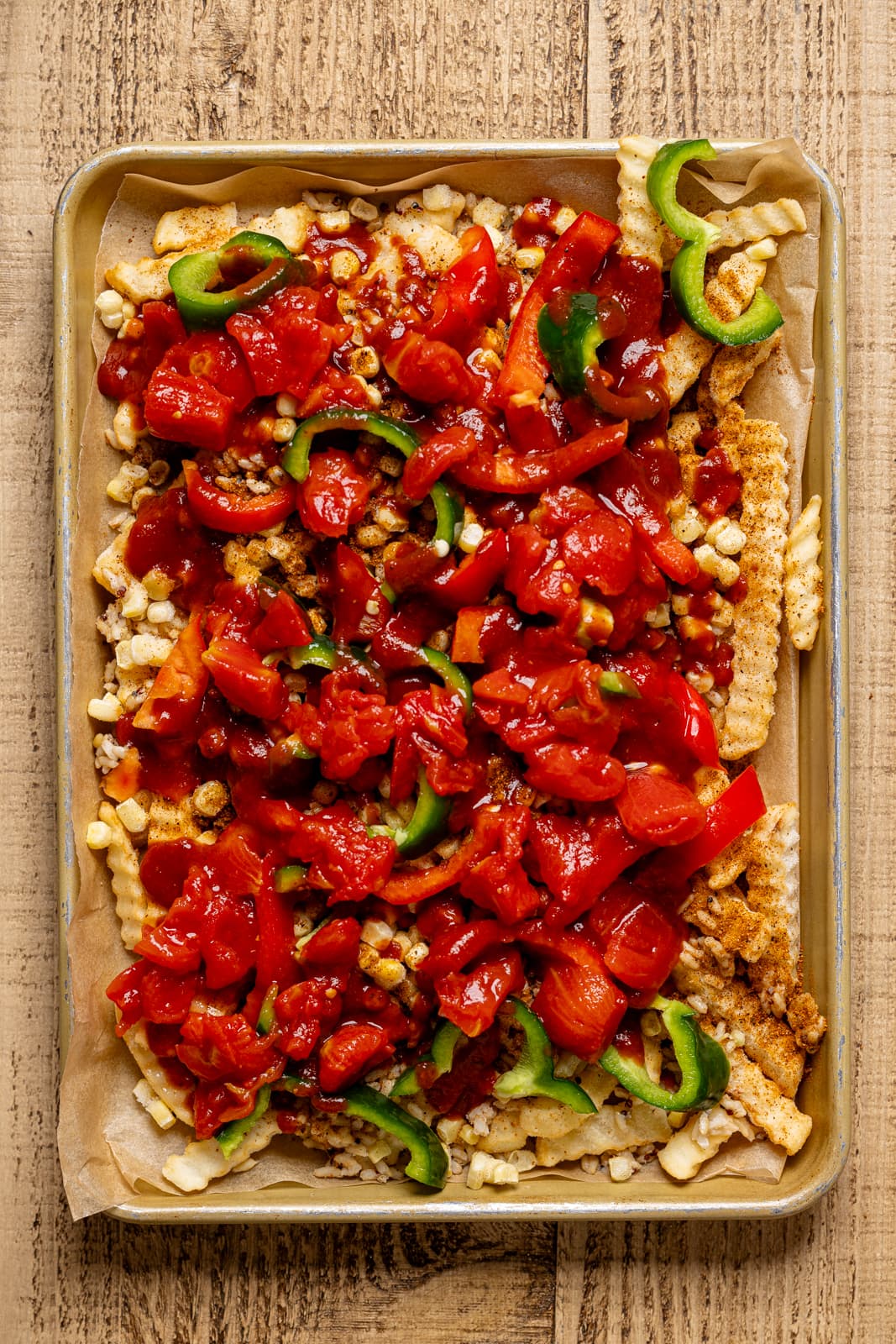 Fries on sheet pan with corn, quinoa, peppers, and diced tomatoes as topping.