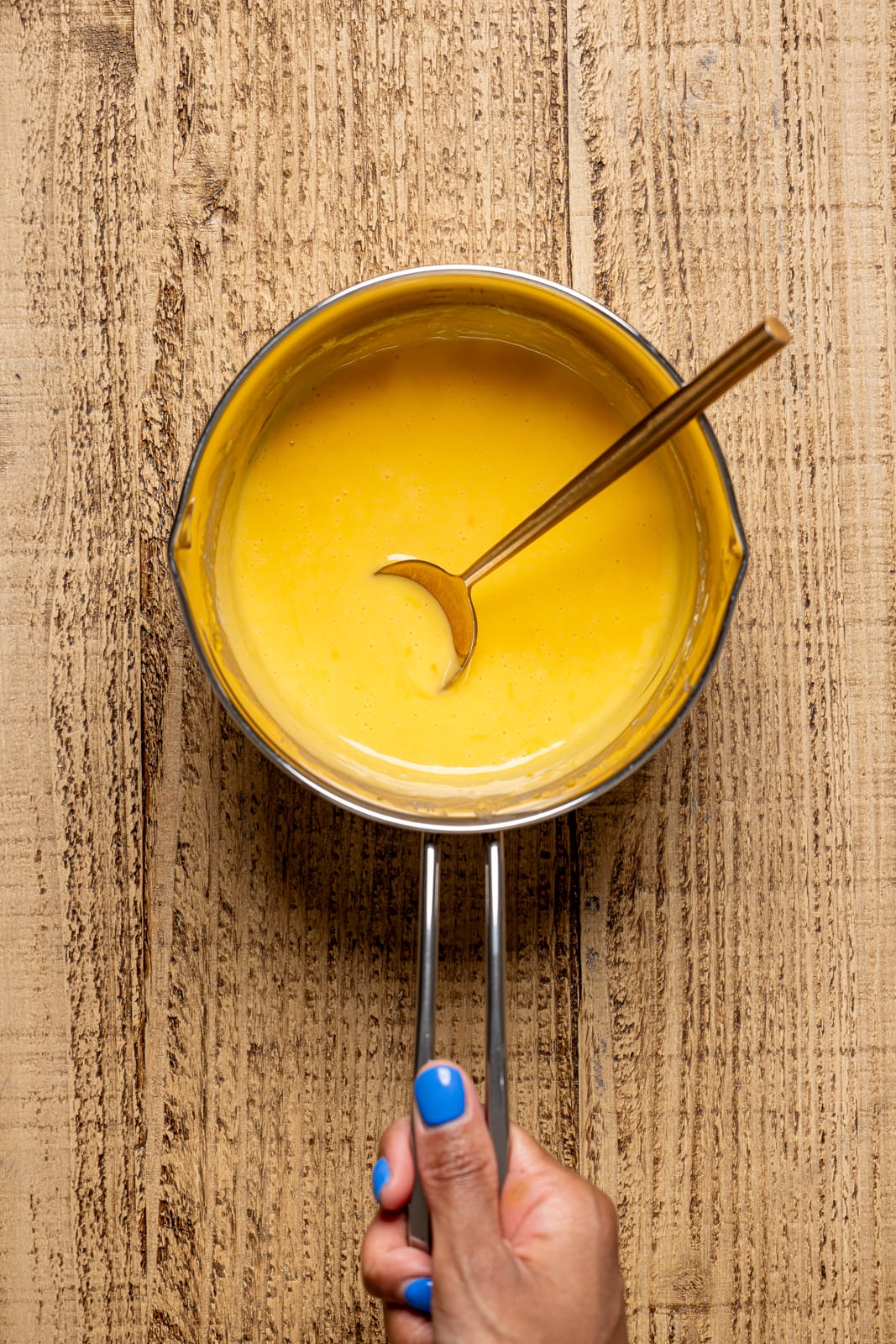 Melted dairy-free nacho cheese in a saucepan with a spoon.