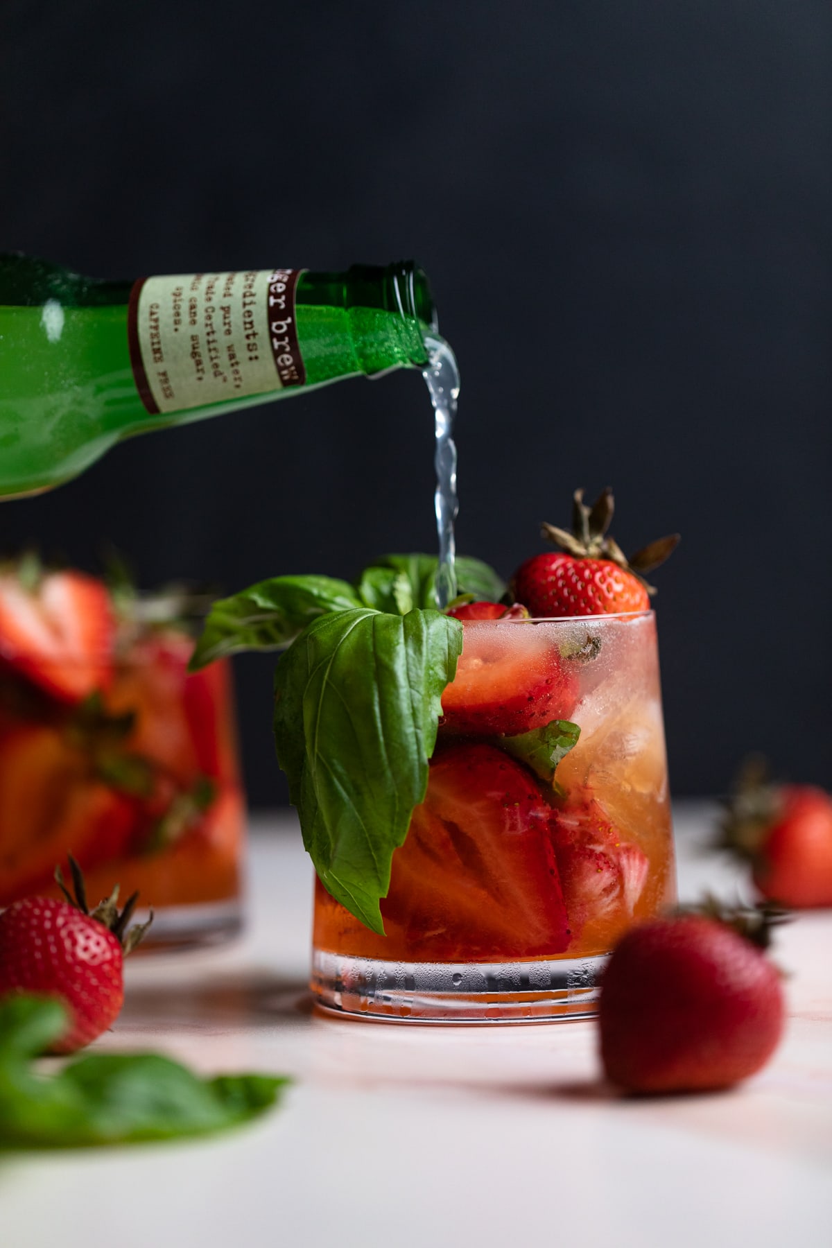 Strawberry Basil Pineapple Mocktail in a glass with fresh strawberries and basil pouring ginger beer on top