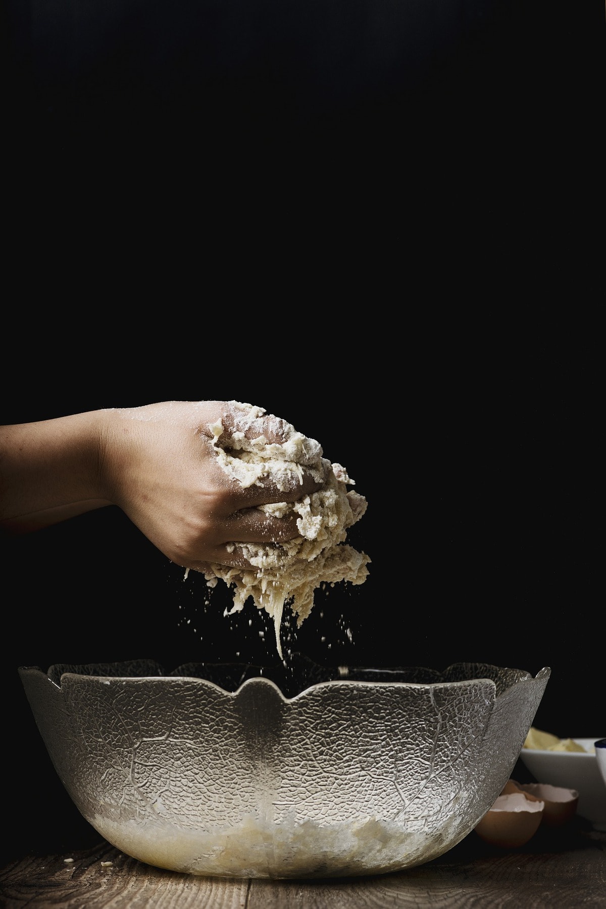 Hands holding dough over a clear bowl.