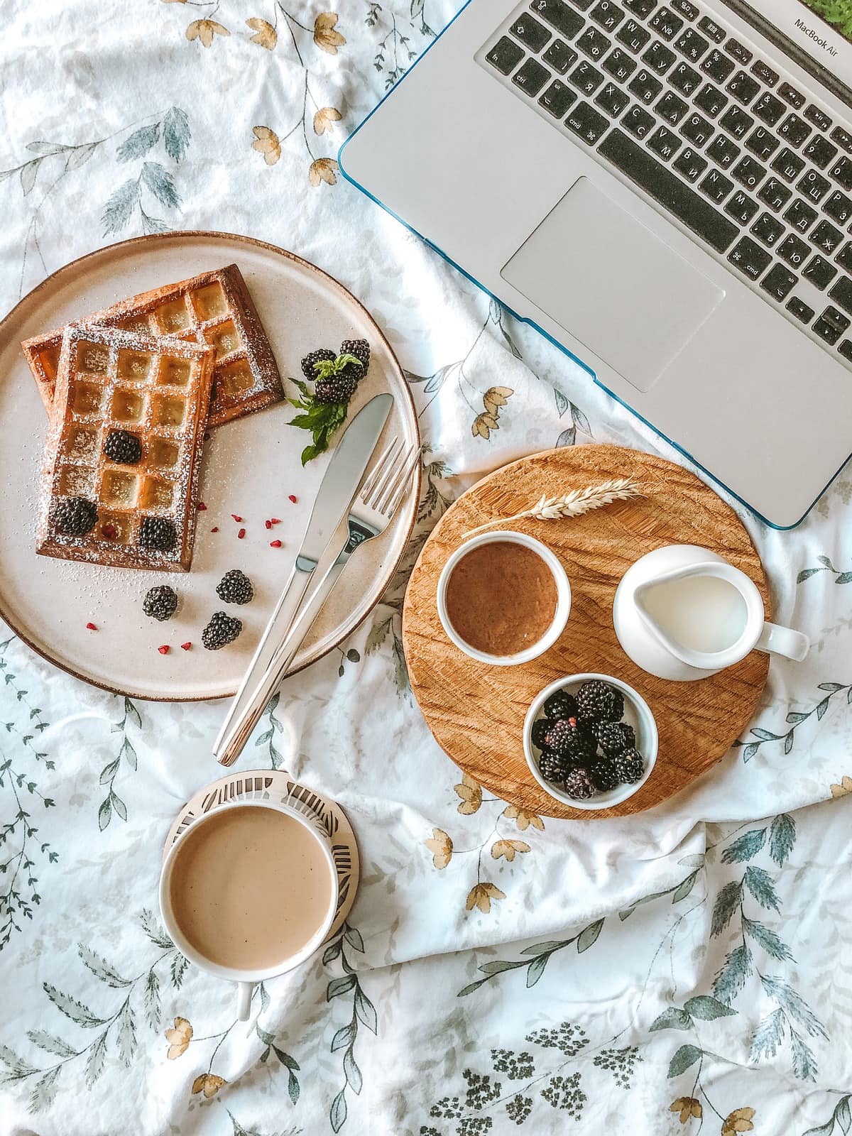 Table set with a plate of waffles, toppings, and a computer.