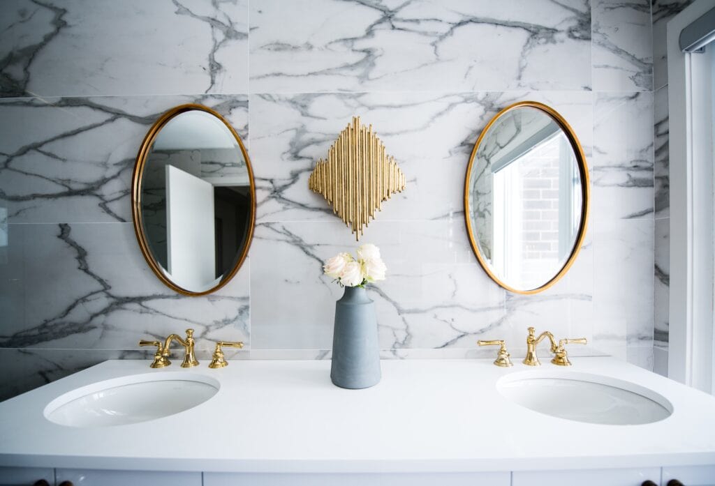 Two oval, gold-framed mirrors hung on a marble wall.