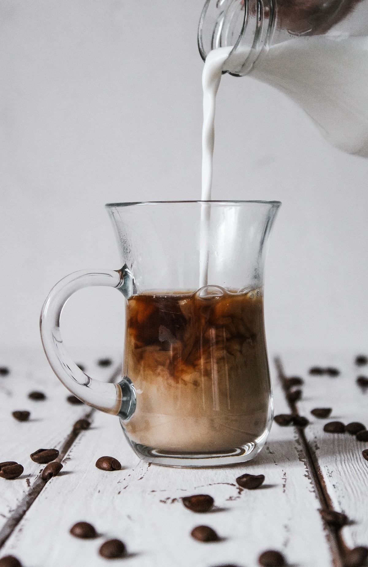 Milk pouring into a glass mug of coffee.