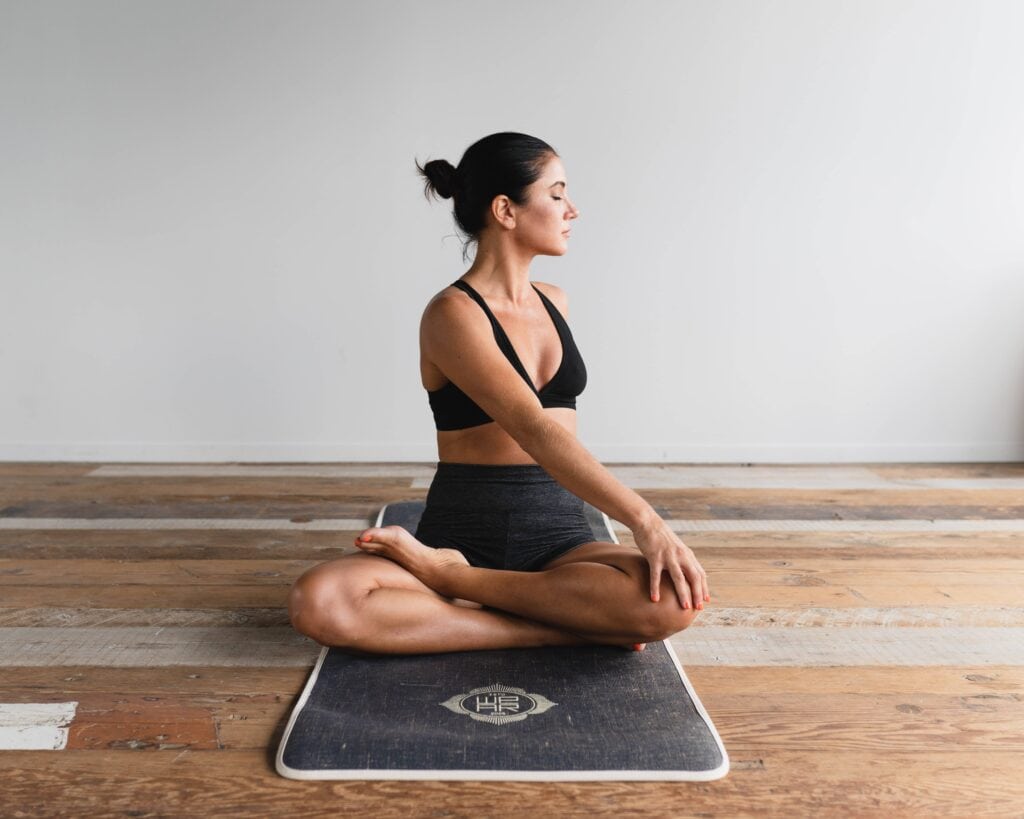 Woman sitting cross-legged on a mat, stretching to one side.